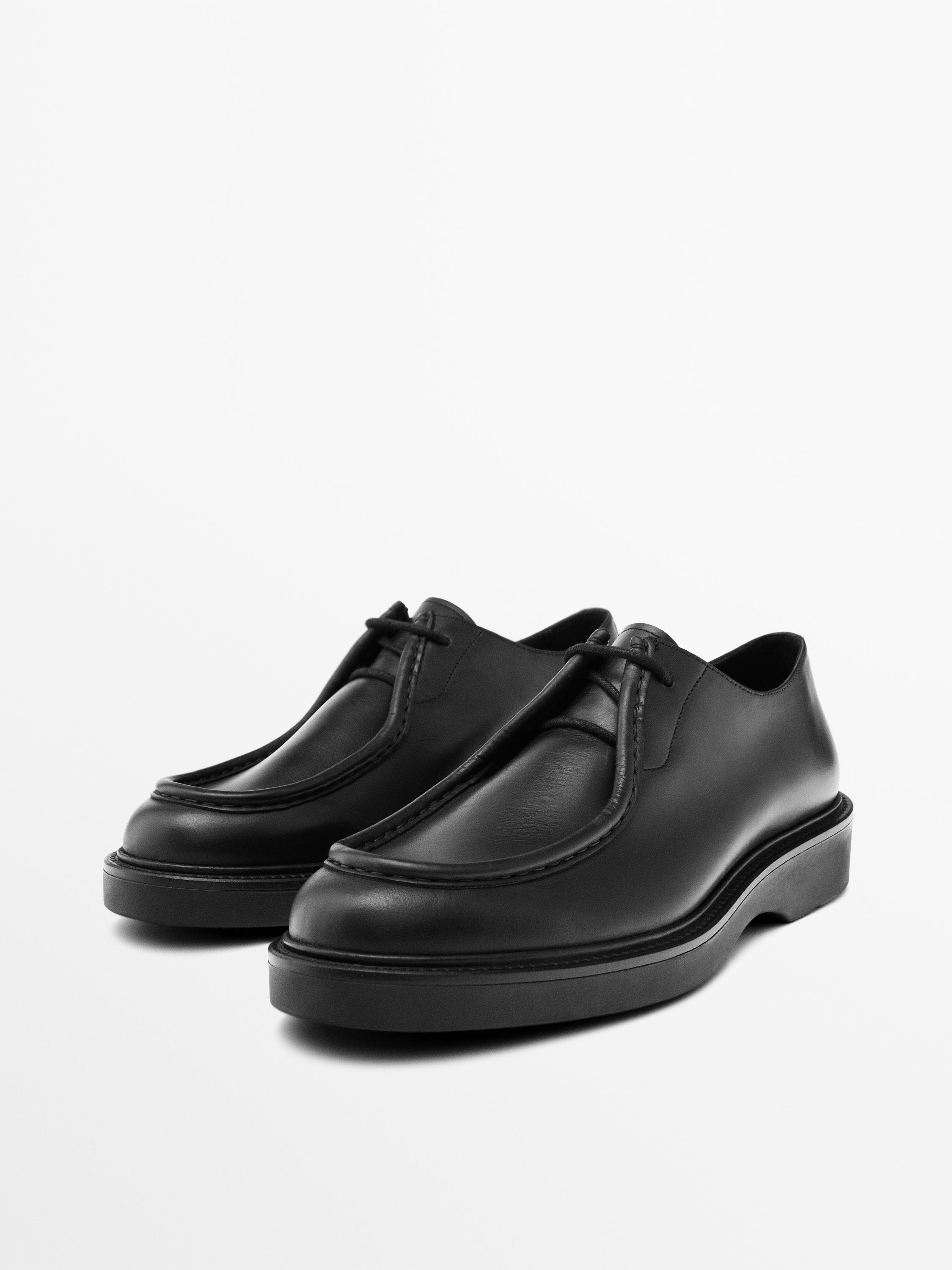 Chaussures noires à lacets avec semelle épaisse et coutures visibles. Vue en angle montrant les deux chaussures.