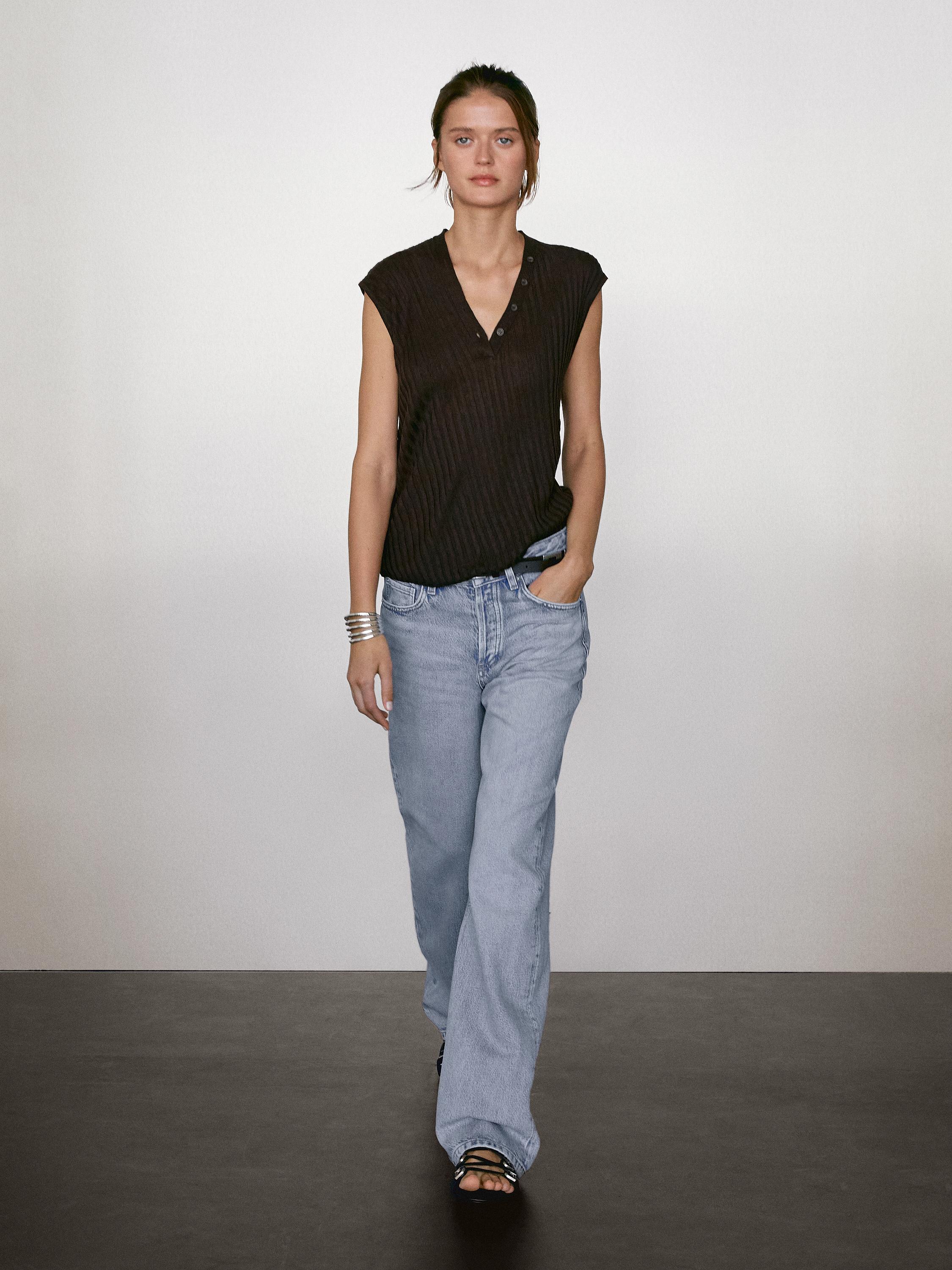 طقم مكون من بلوزة سوداء بدون أكمام بأزرار وجينز أزرق فاتح بقصة مستقيمة.