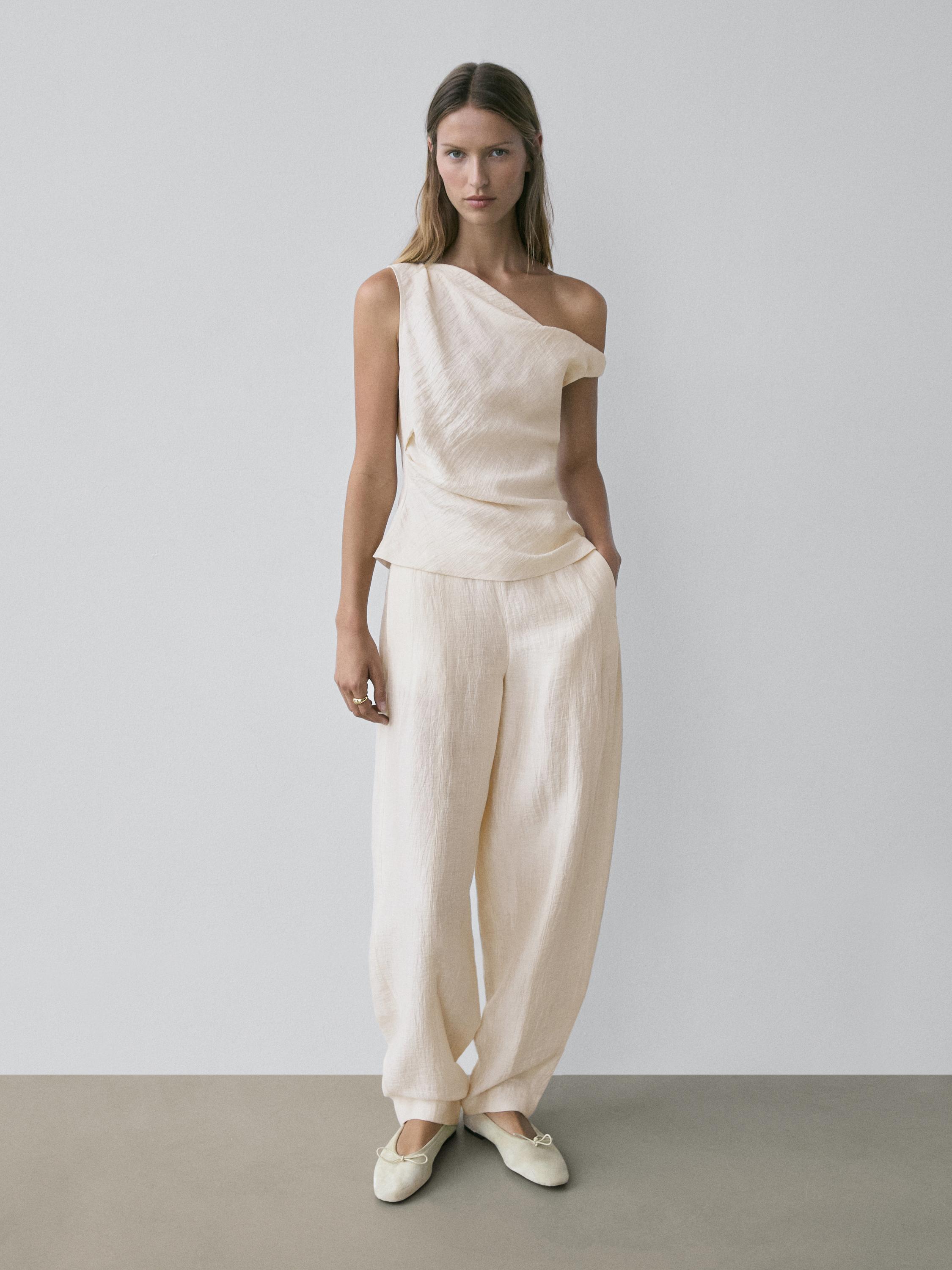 Комплект из асимметричной блузки и широких брюк светло-бежевого цвета, с туфлями без каблука в тон.