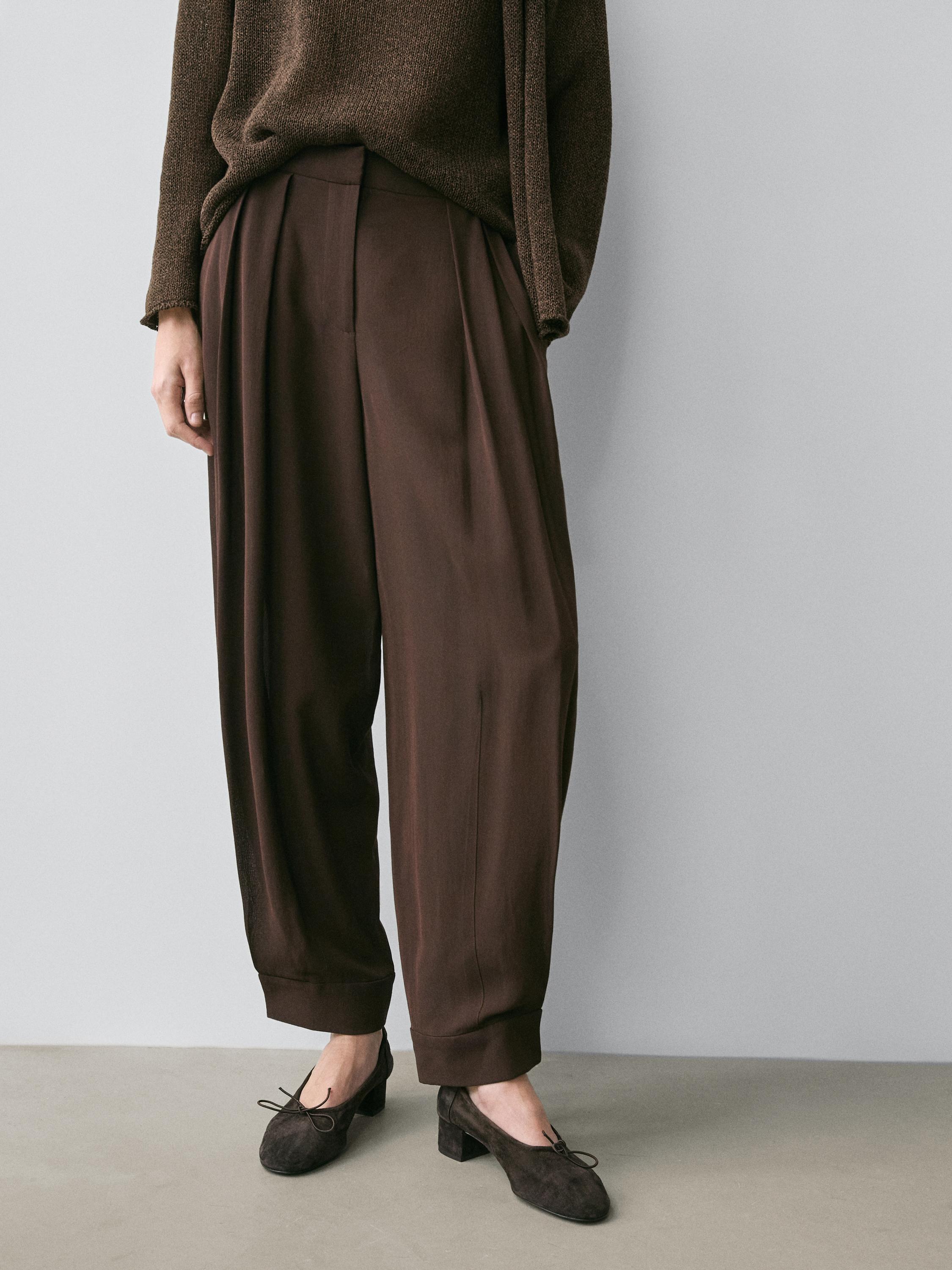 Brown pleated balloon pants set with button detail, paired with a brown sweater and dark shoes.