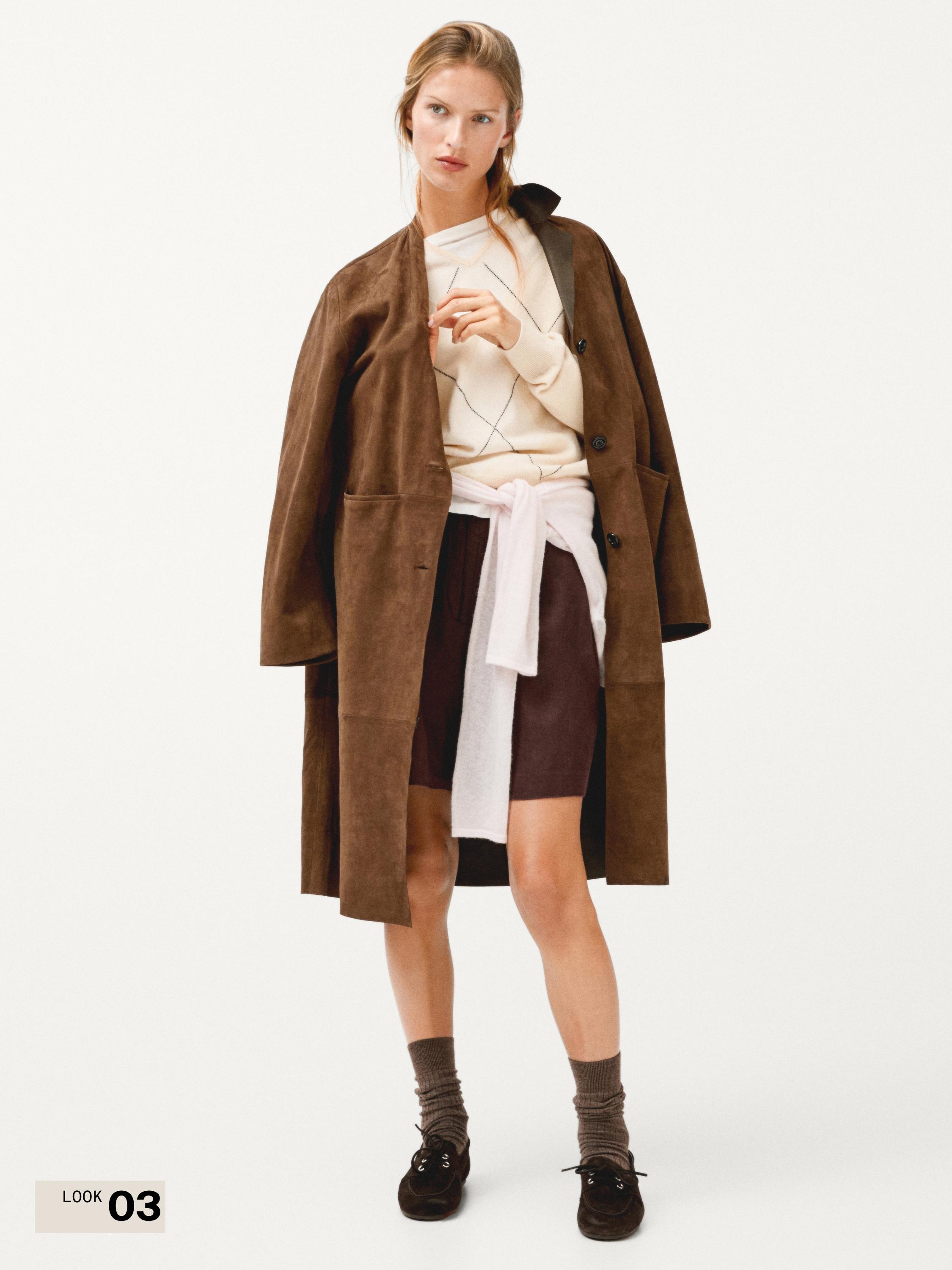 طقم سترة بنية، سويتر بيج بتصميم هندسي، تنورة بنية، سويتر أبيض مربوط وجوارب رمادية.