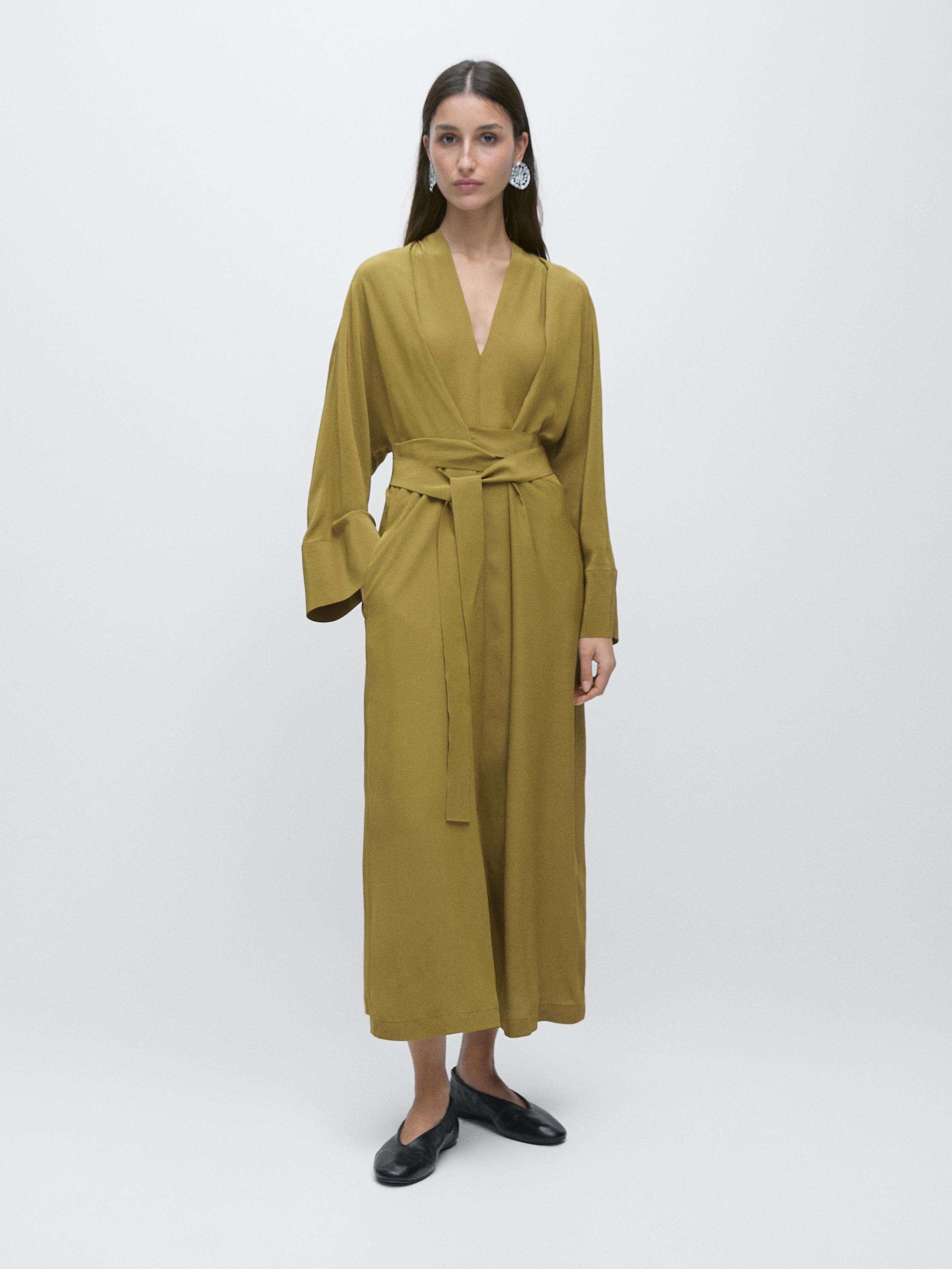 فستان طويل انسيابي أخضر بياقة على شكل V وأكمام طويلة وحزام معقود على الخصر.