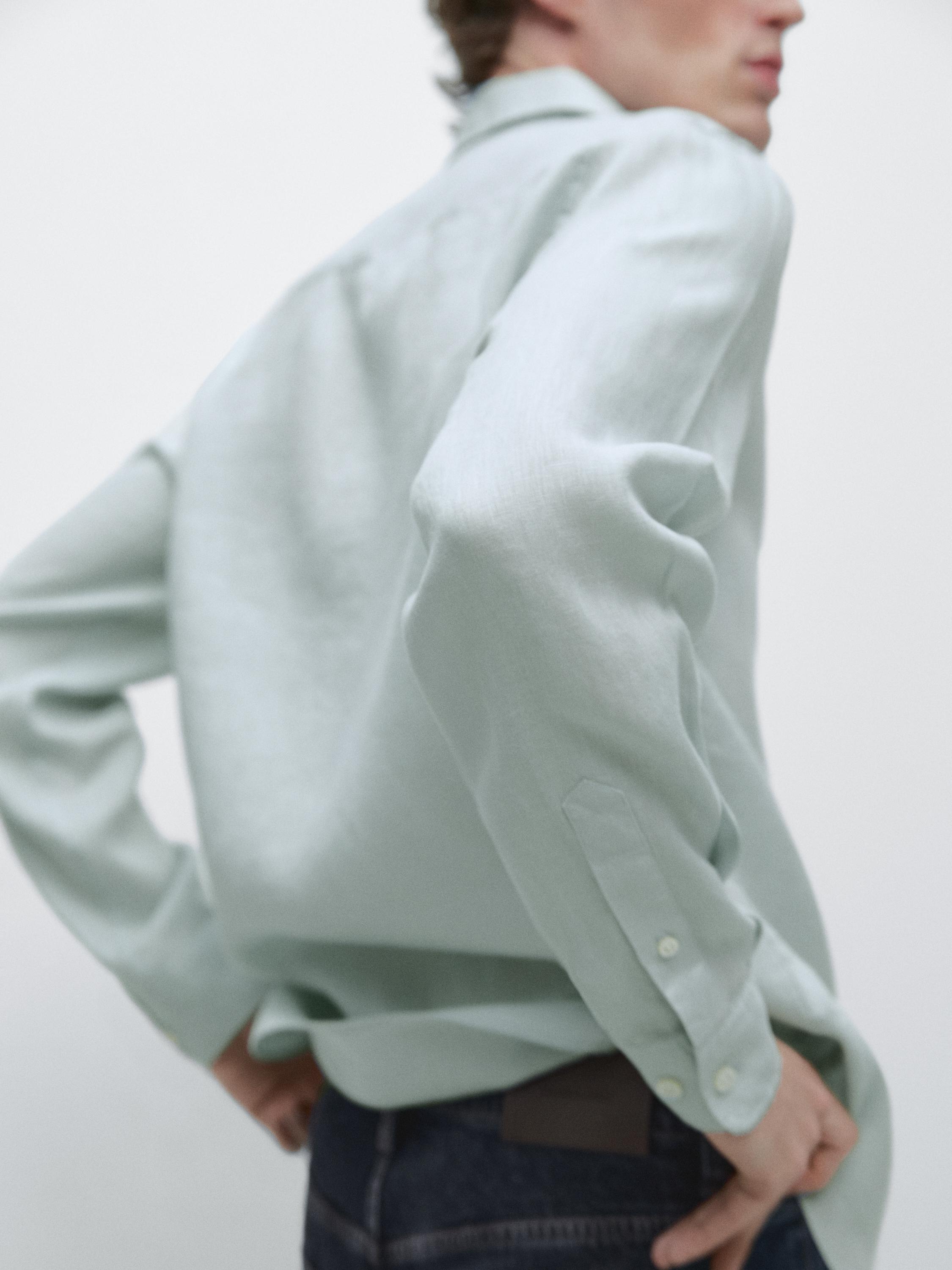 Plano medio de la manga y espalda de camisa verde claro de manga larga con puños abotonados.