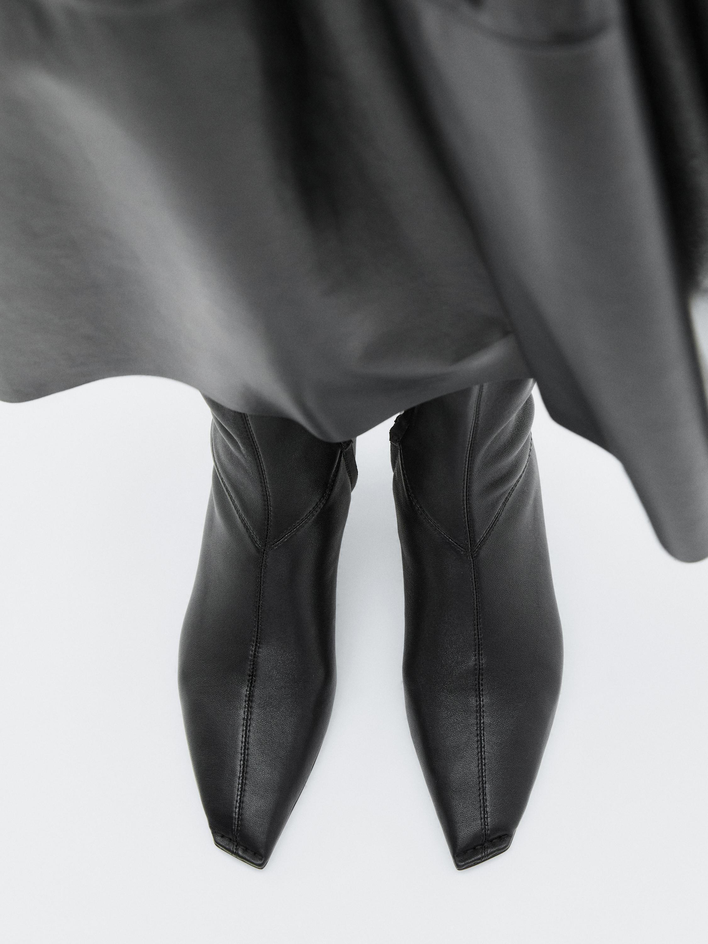 لقطة متوسطة لبوت أسود ذي مقدمة مربعة تحت تنورة سوداء.