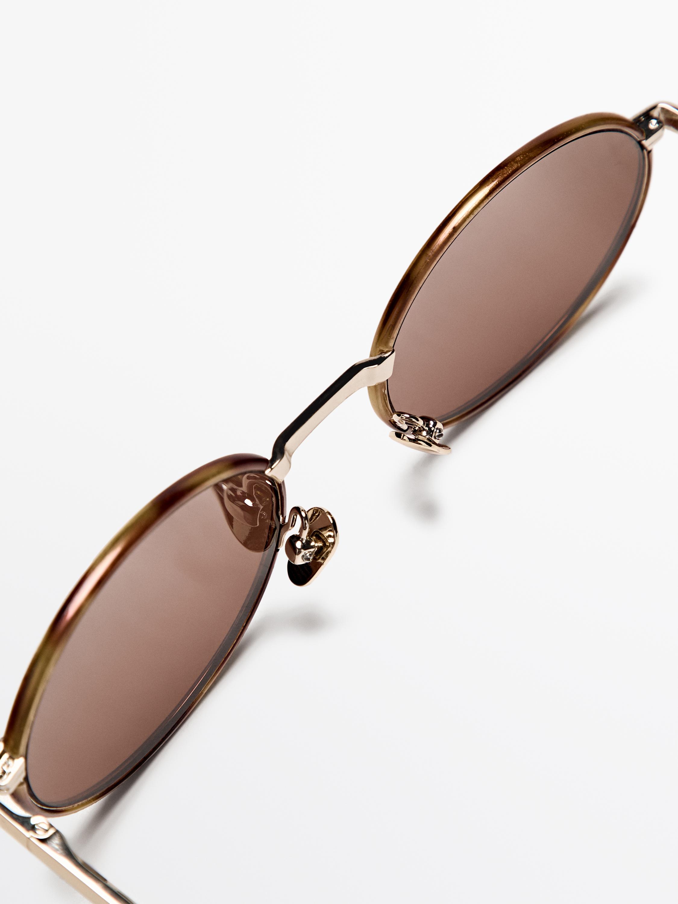 Gros plan sur des lunettes de soleil marron avec une monture métallique dorée et des verres ovales.