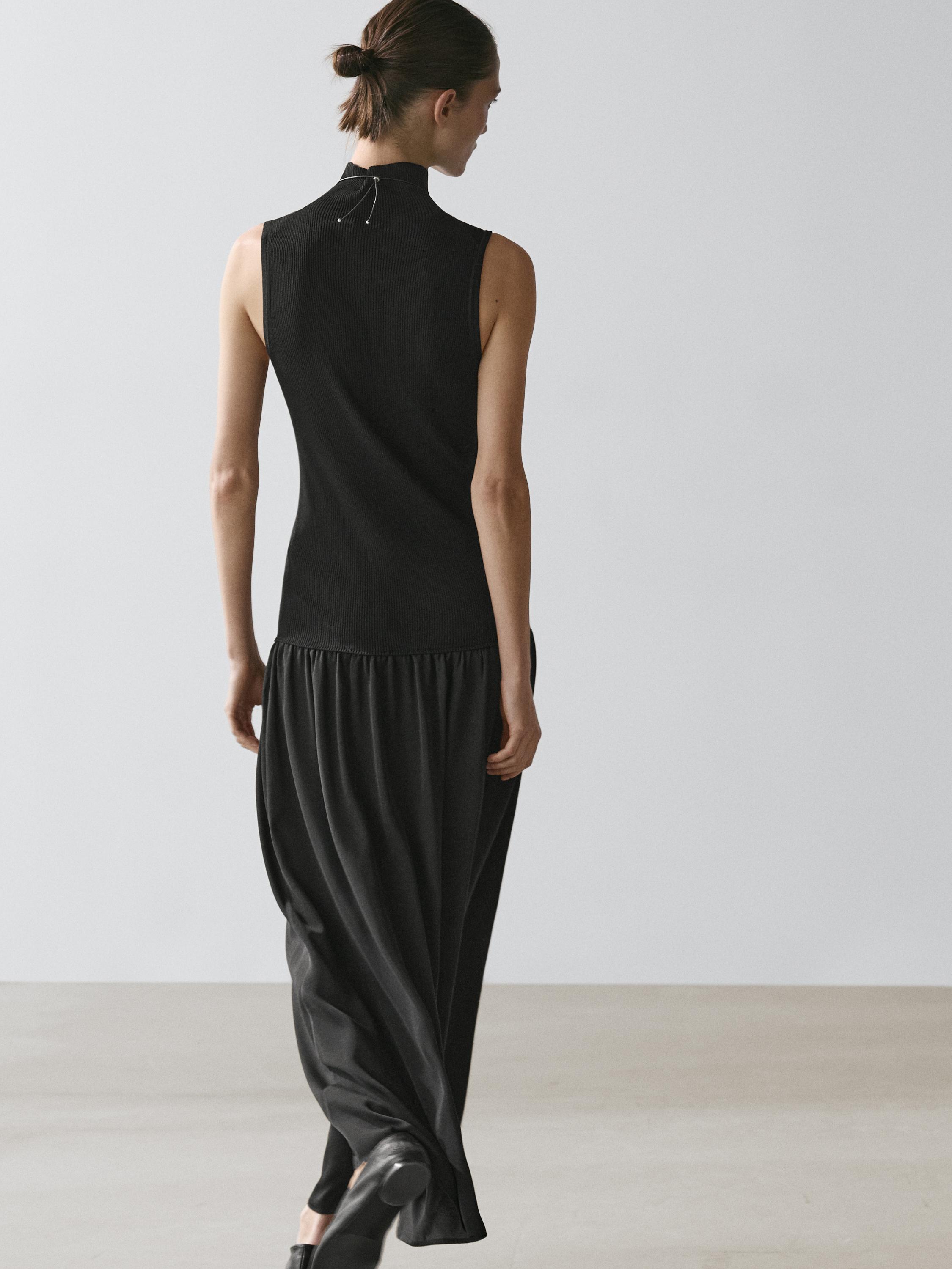 Ensemble robe noire sans manches, longueur midi, avec col montant et jupe fluide. Vue arrière.
