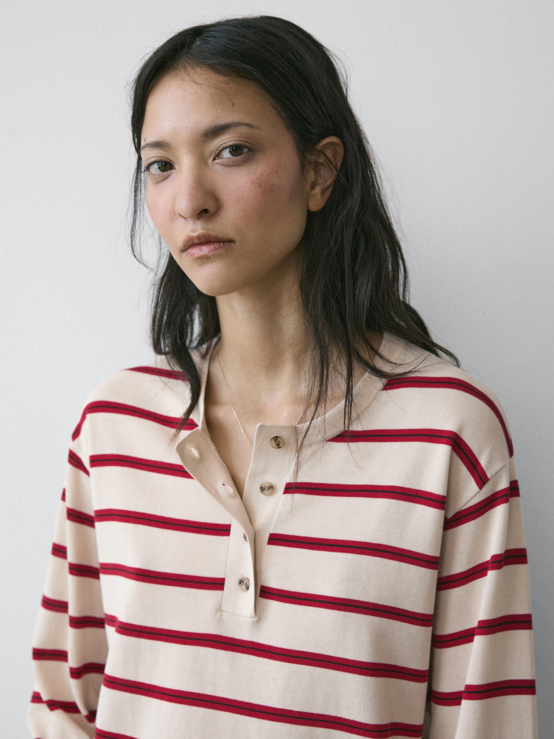 "เสื้อเจอร์ซีย์ถักสีเบจลายทางสีแดงและคอปกแบบมีกระดุมที่มองเห็นได้"