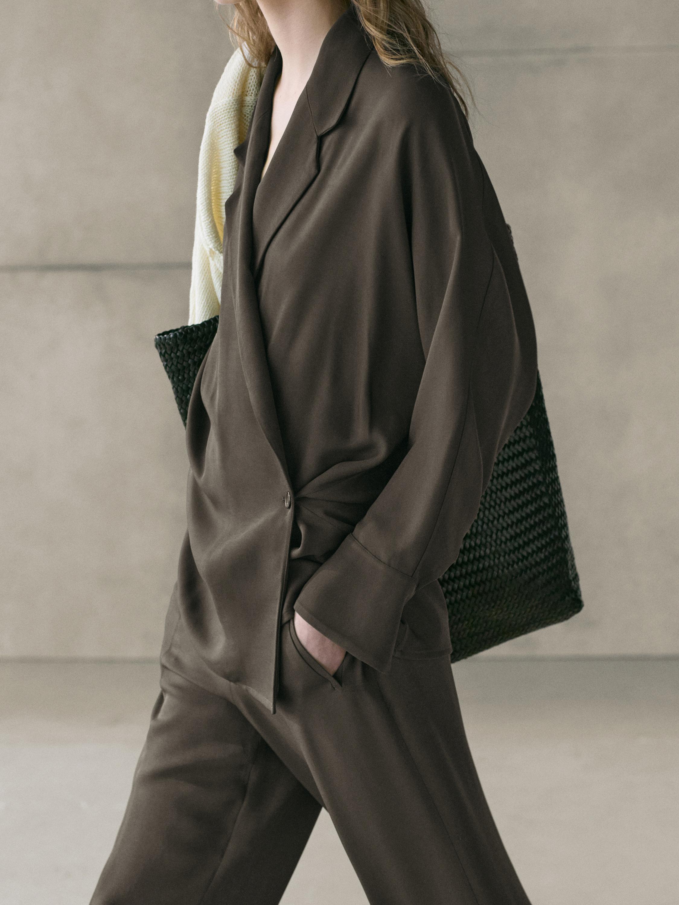 Mezzo piano di blazer verde-grigiastro con revers e tasche laterali, abbinato a pantaloni coordinati.