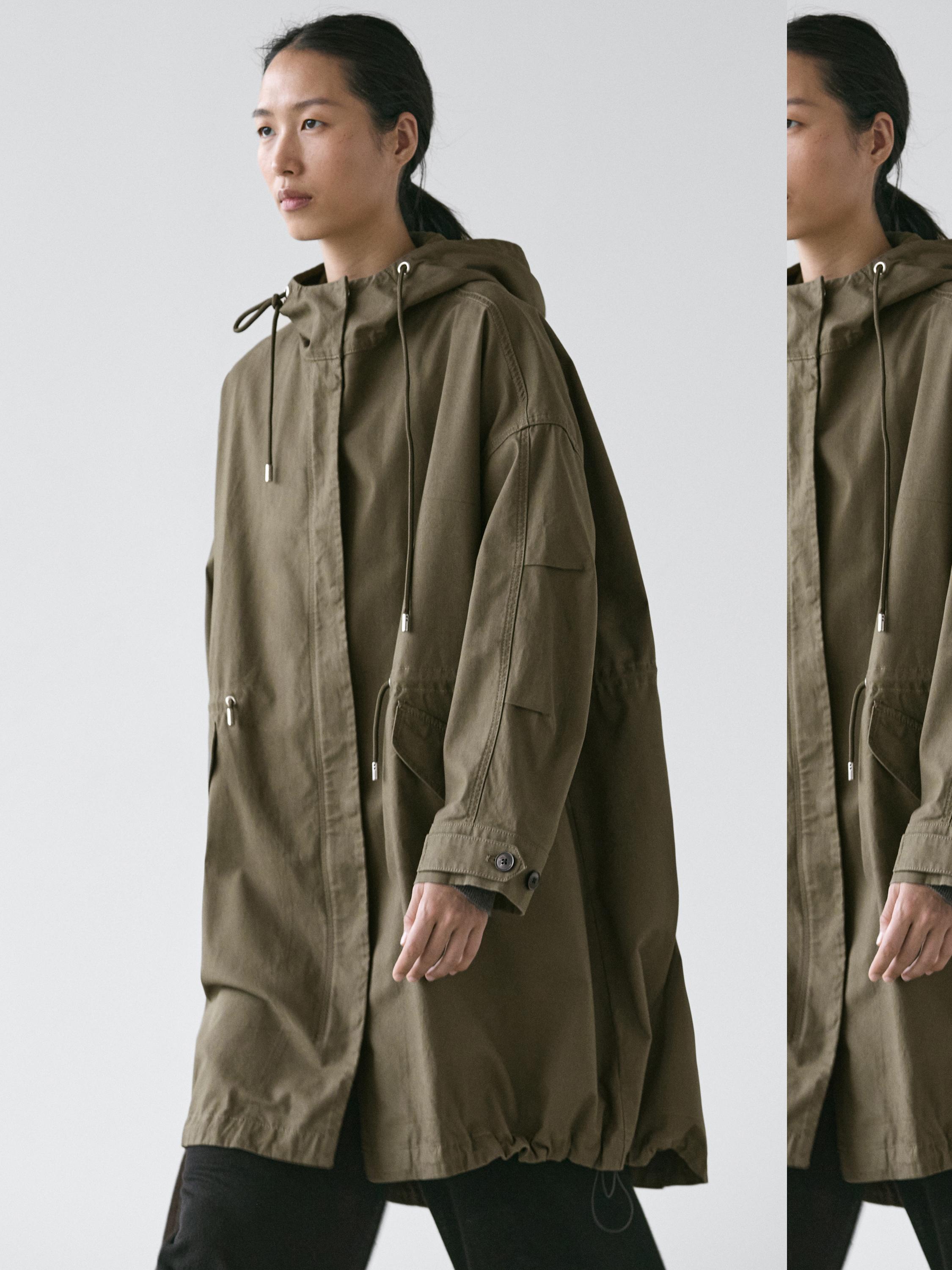 Khaki coat set with a hood, adjustable drawstrings, and side pockets, over black pants.