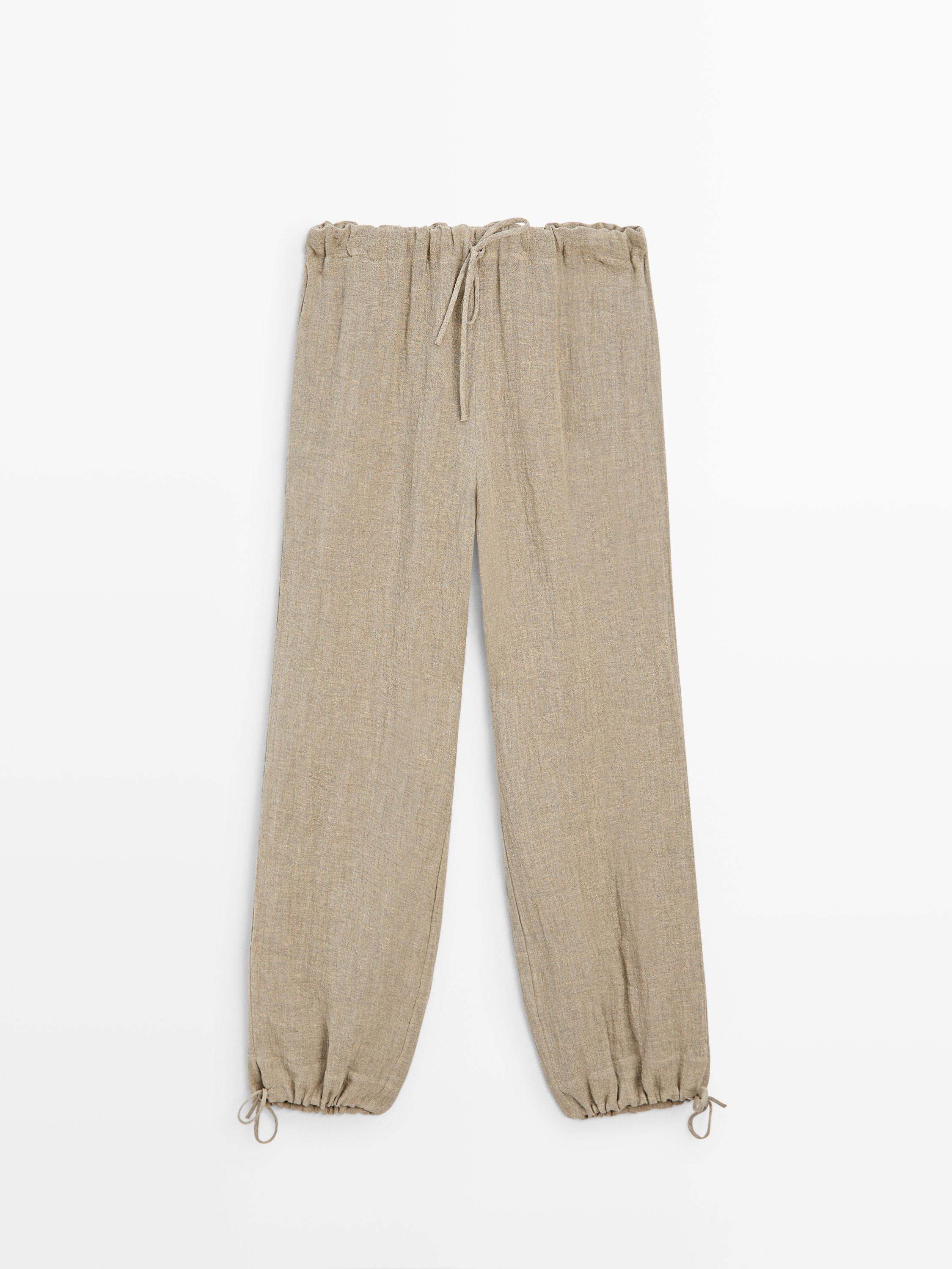 Vista frontal de pantalón bombacho color piedra con cintura y tobillos elásticos ajustables con cordón.