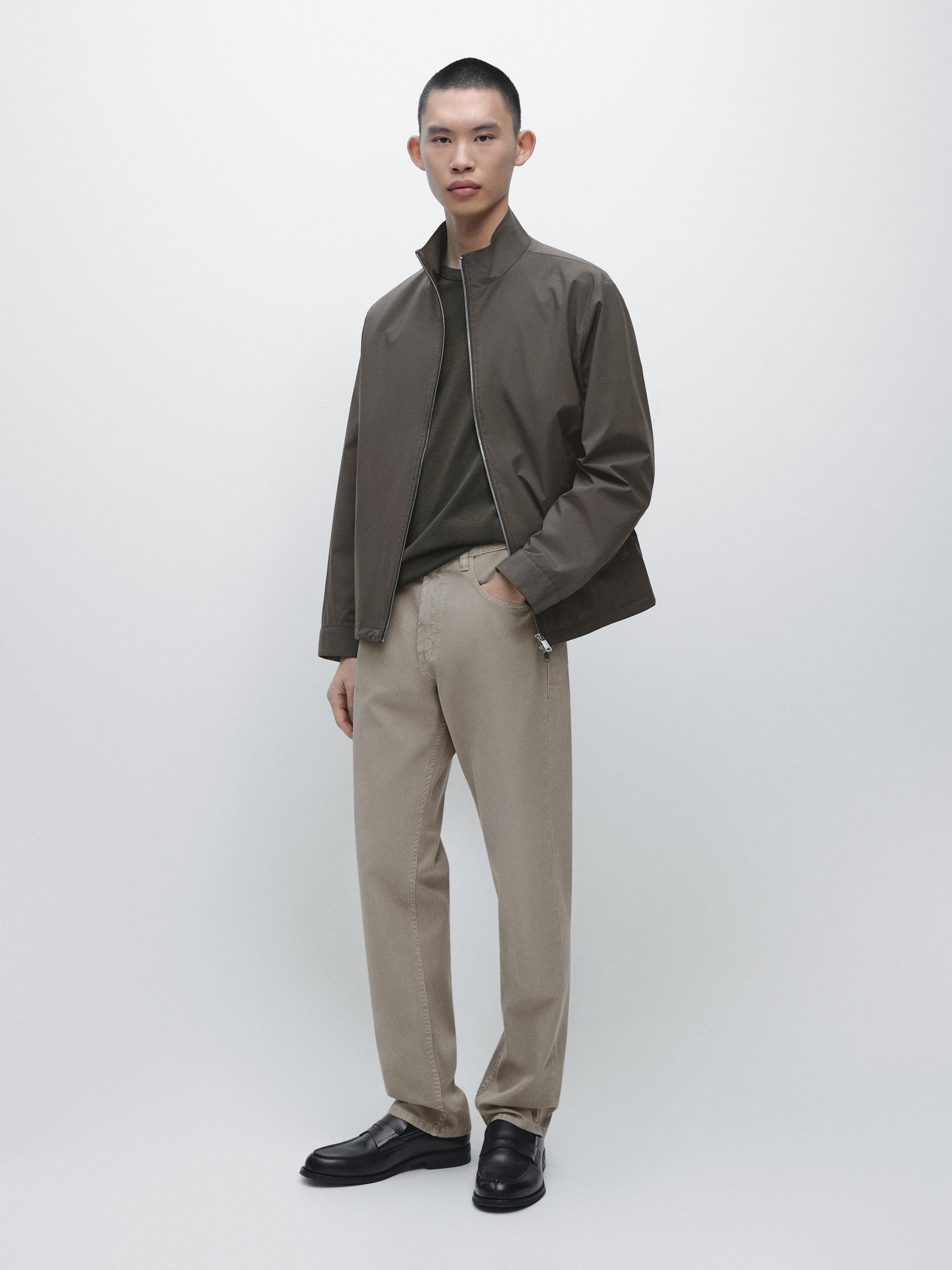 Komplet smeđe jakne s patentnim zatvaračem, tamnozelene majice i opuštenih svijetlozelenih traperica, crne cipele.