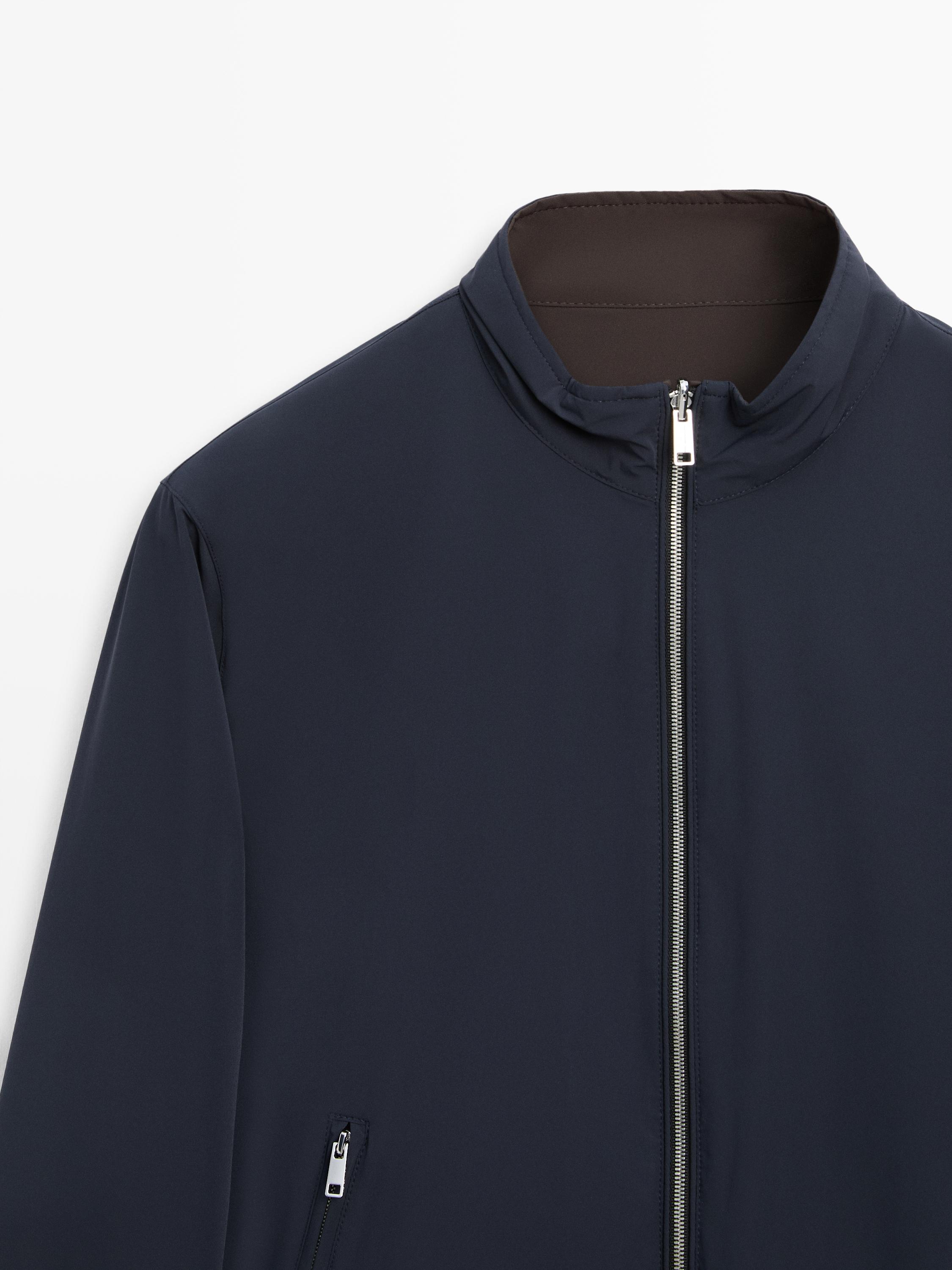 "Mid-shot of a navy blue jacket with a front zipper and high collar. Visible side zipper pocket."