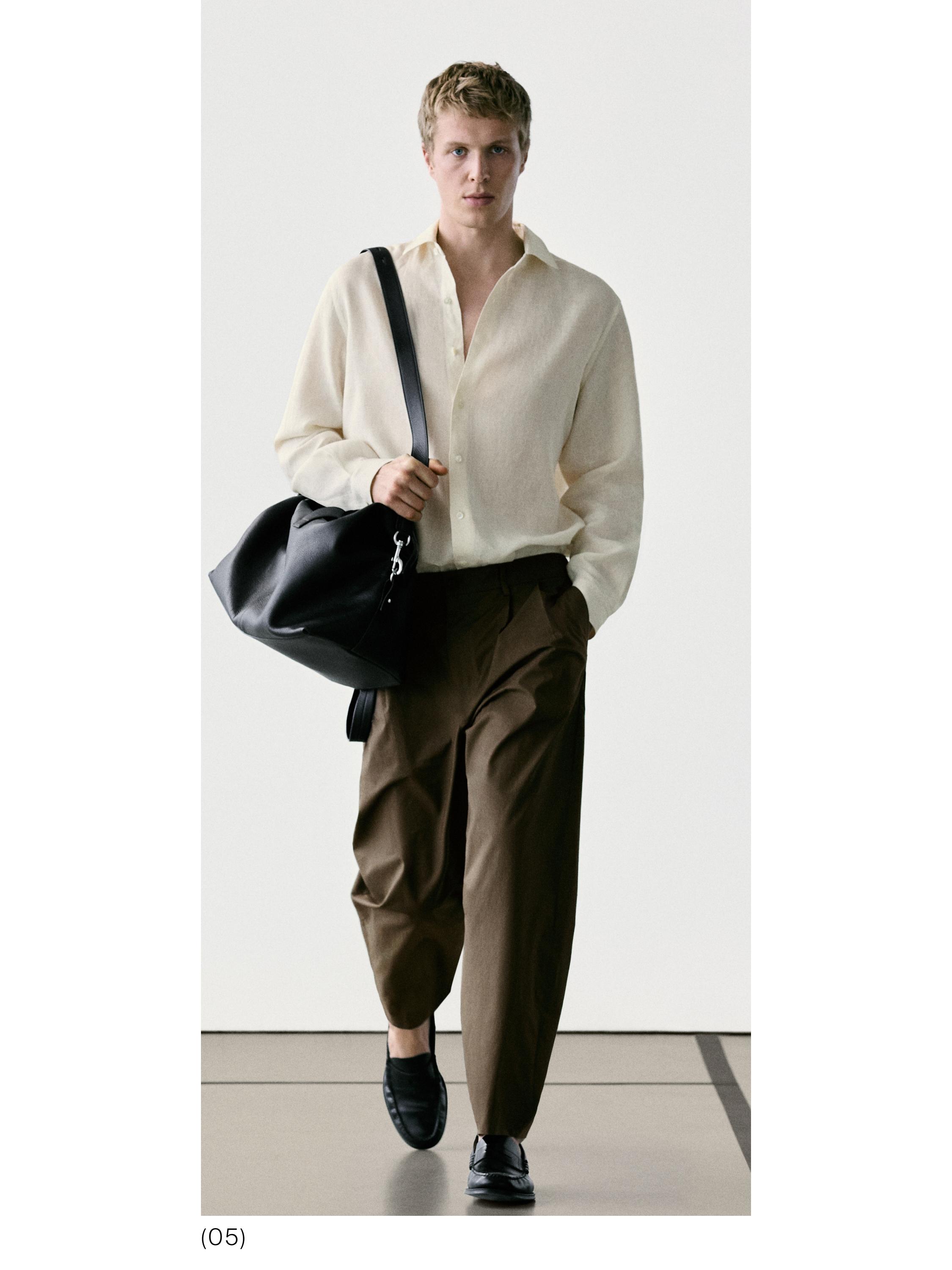 Beige set van een lange mouwen overhemd en een losse bruine broek met plooien. Ze draagt een zwarte tas en zwarte loafers.