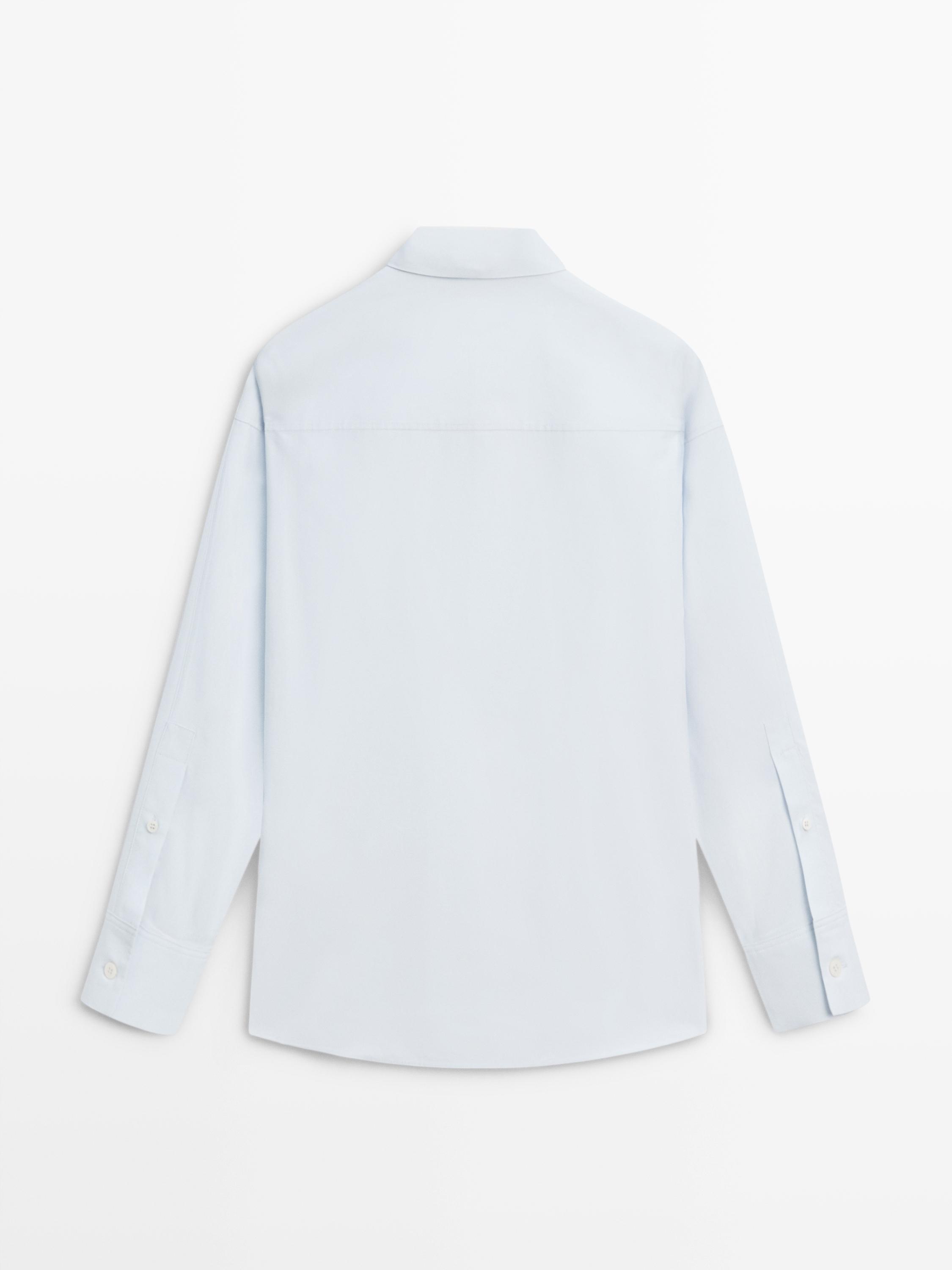 Düğmeli manşetli, uzun kollu açık mavi gömleğin arka görünümü.