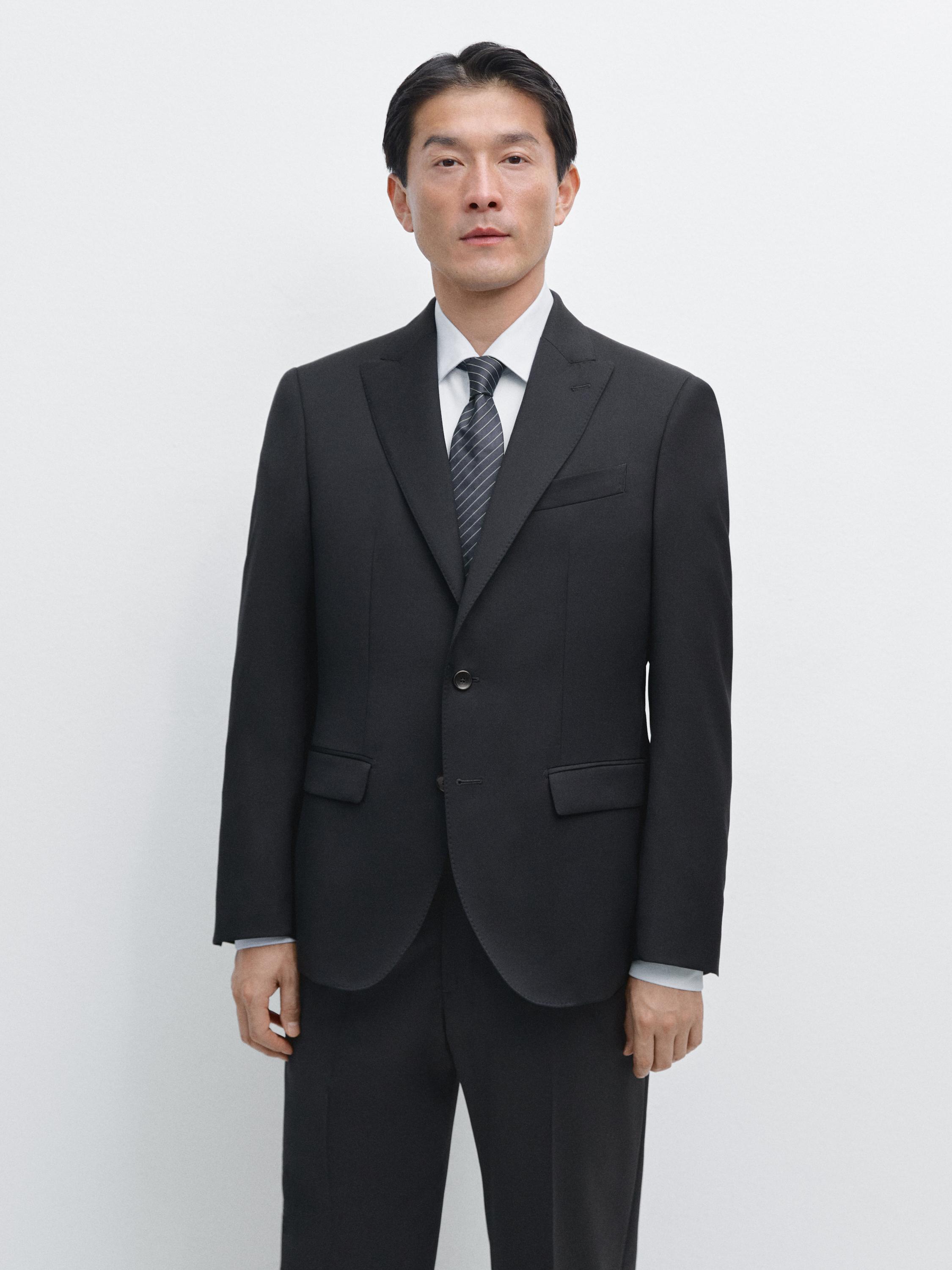 Σετ σκούρο μπλε κοστούμι με σακάκι δύο κουμπιών, κλασικά πέτα και τσέπες με καπάκι, συνδυασμένο με ριγέ γραβάτα.