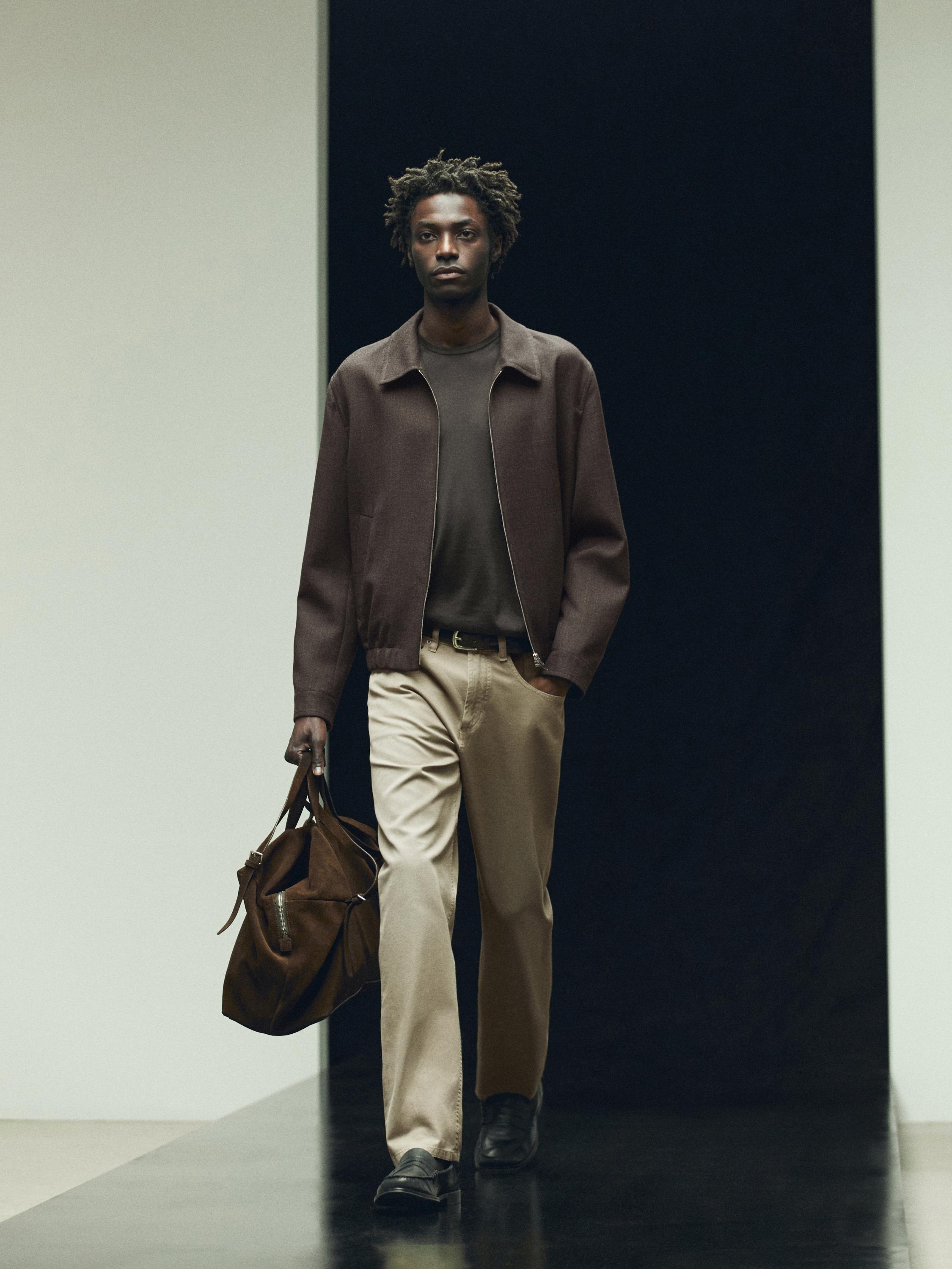 Ensemble composé d'une veste marron, d'un t-shirt foncé, d'un pantalon beige et d'un sac marron.