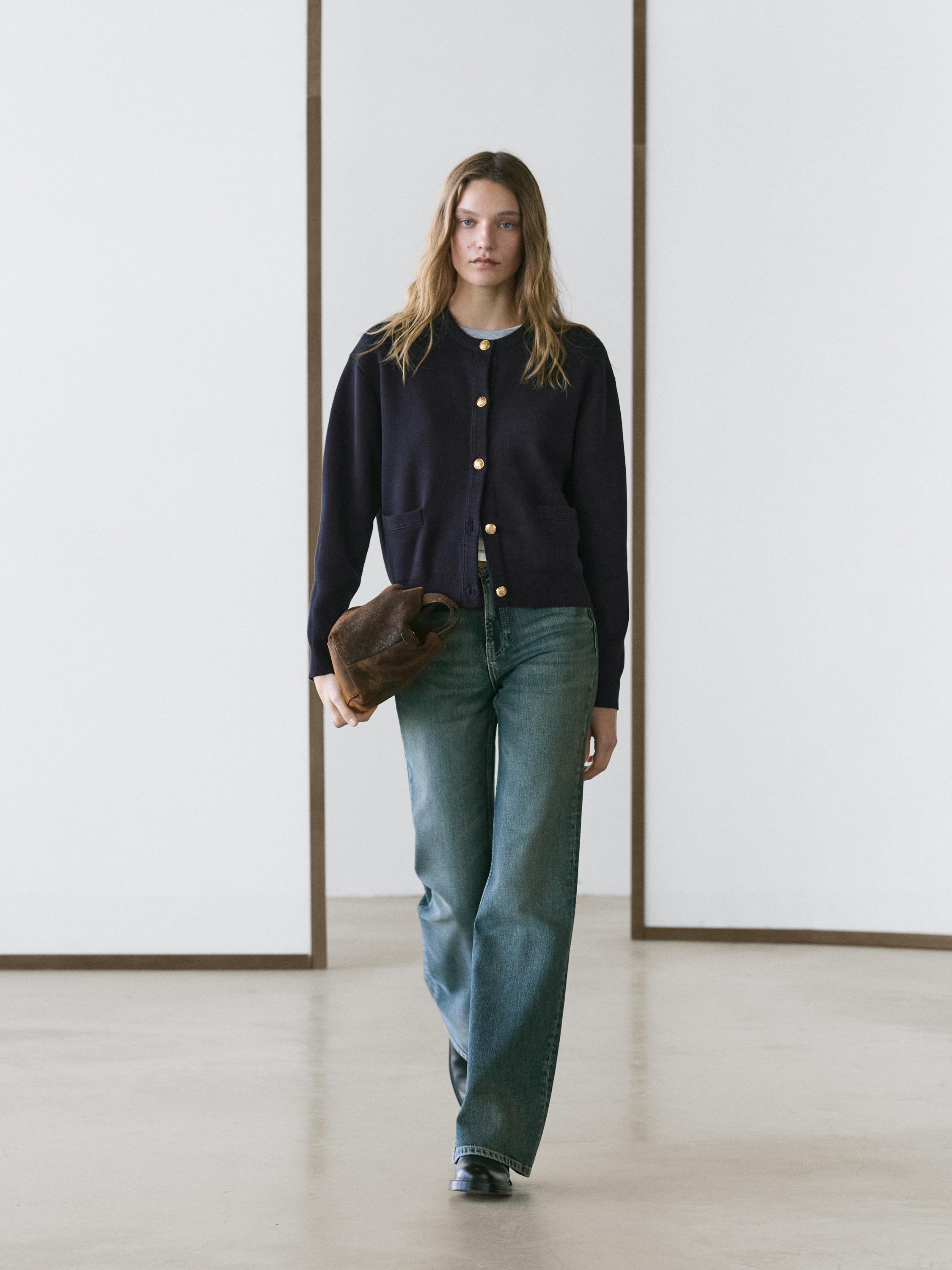 Conjunto de cárdigan azul marino con botones dorados y bolsillos frontales, pantalones vaqueros anchos y zapatos negros.