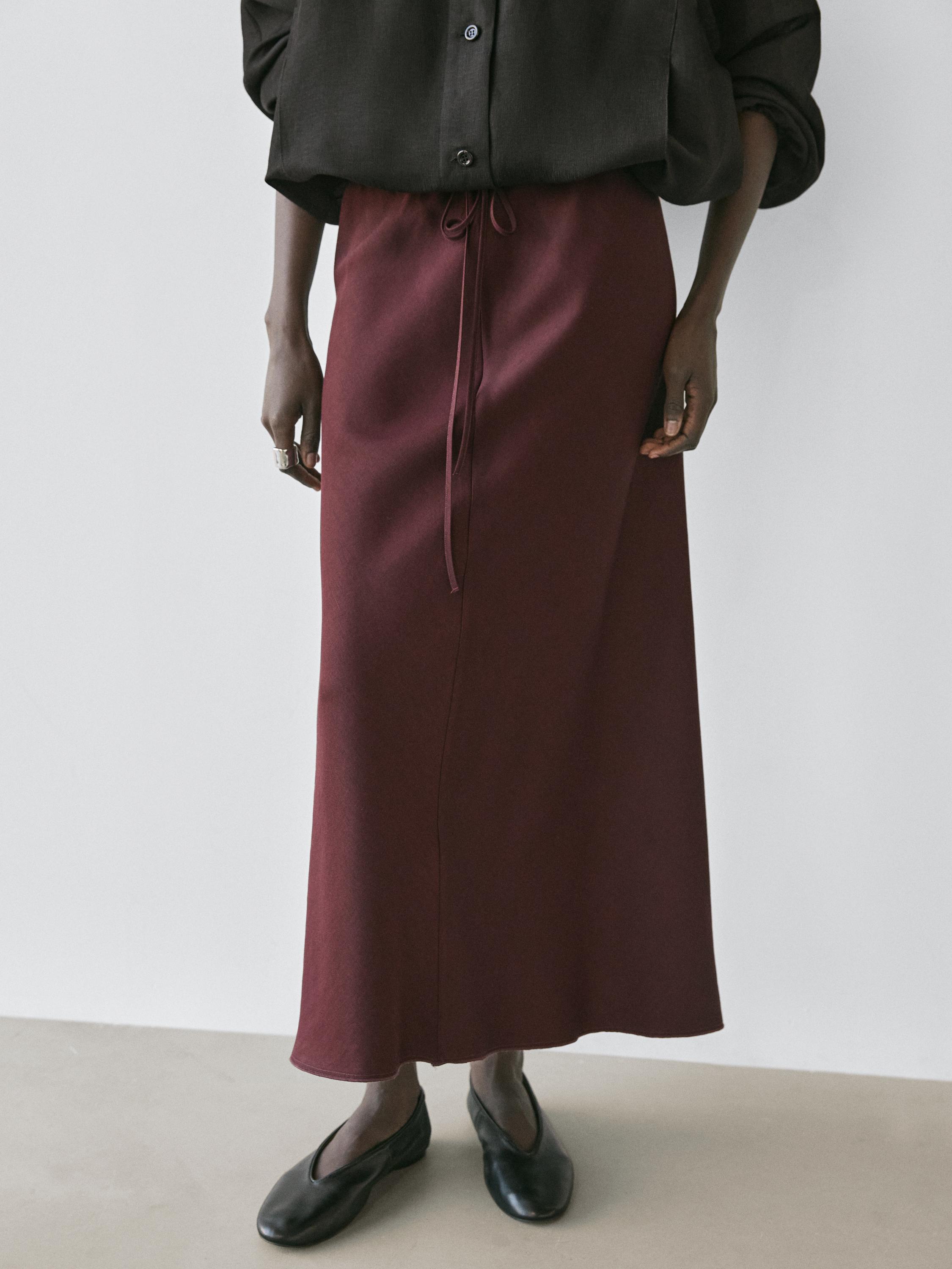 Ensemble jupe midi bordeaux avec nœud à la taille et chemisier noir à manches longues.