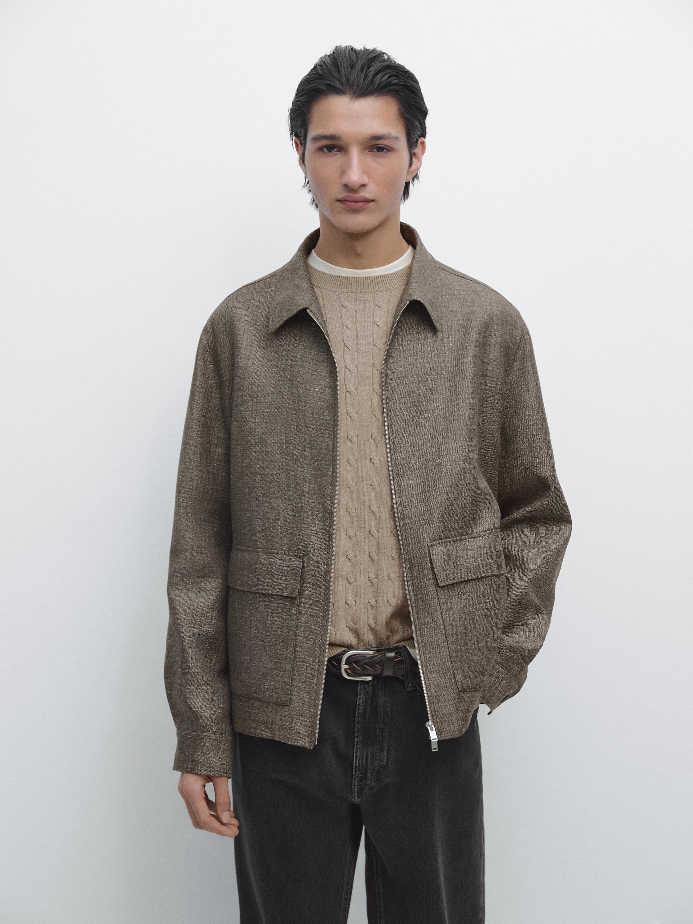 Conjunto de chaqueta corta marrón con bolsillos frontales y cremallera, suéter beige de punto trenzado y pantalones oscuros.