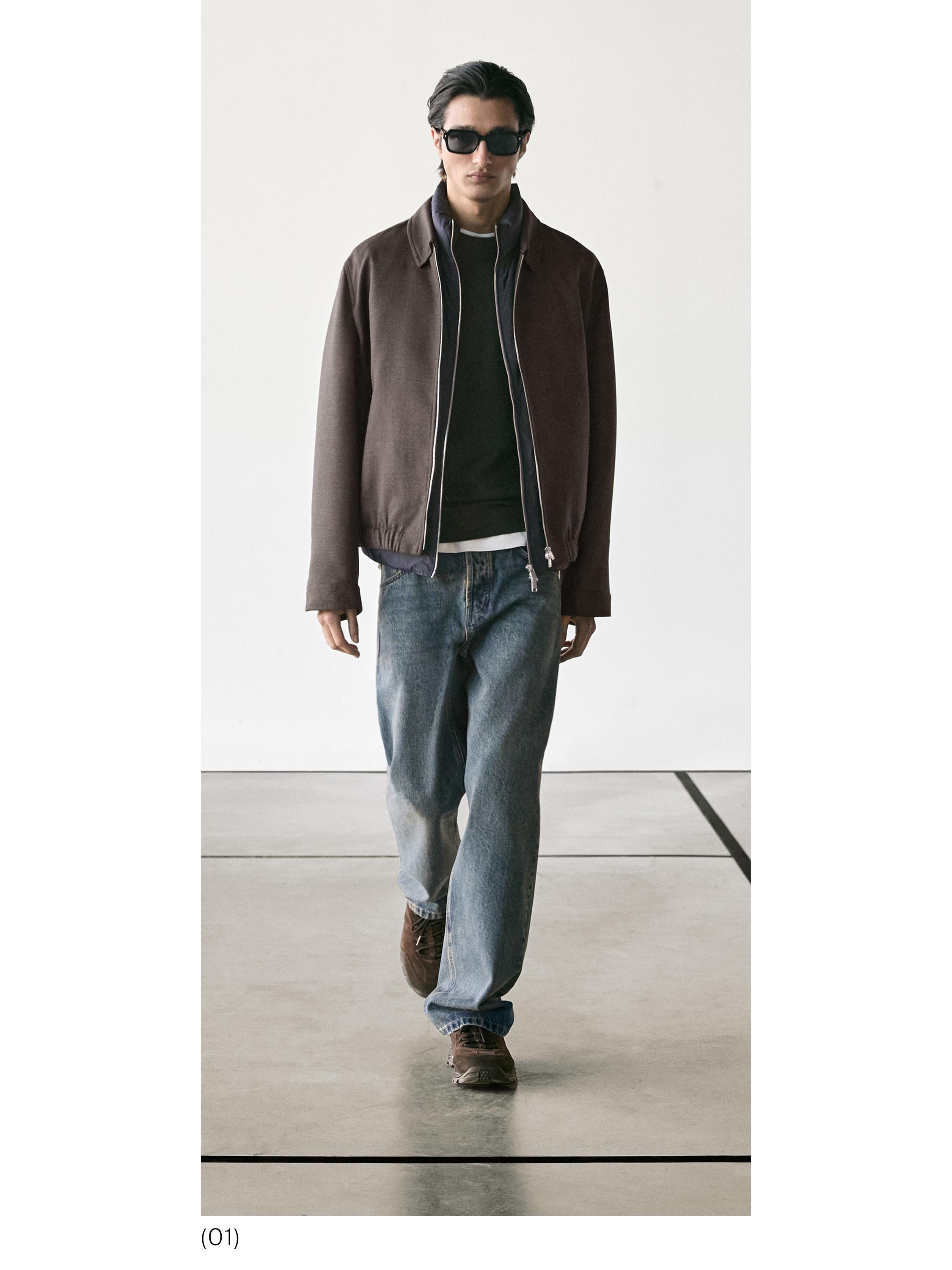 Brūna jaka ar rāvējslēdzēju, tumšs džemperis, zili džinsi un brūnas kurpes.