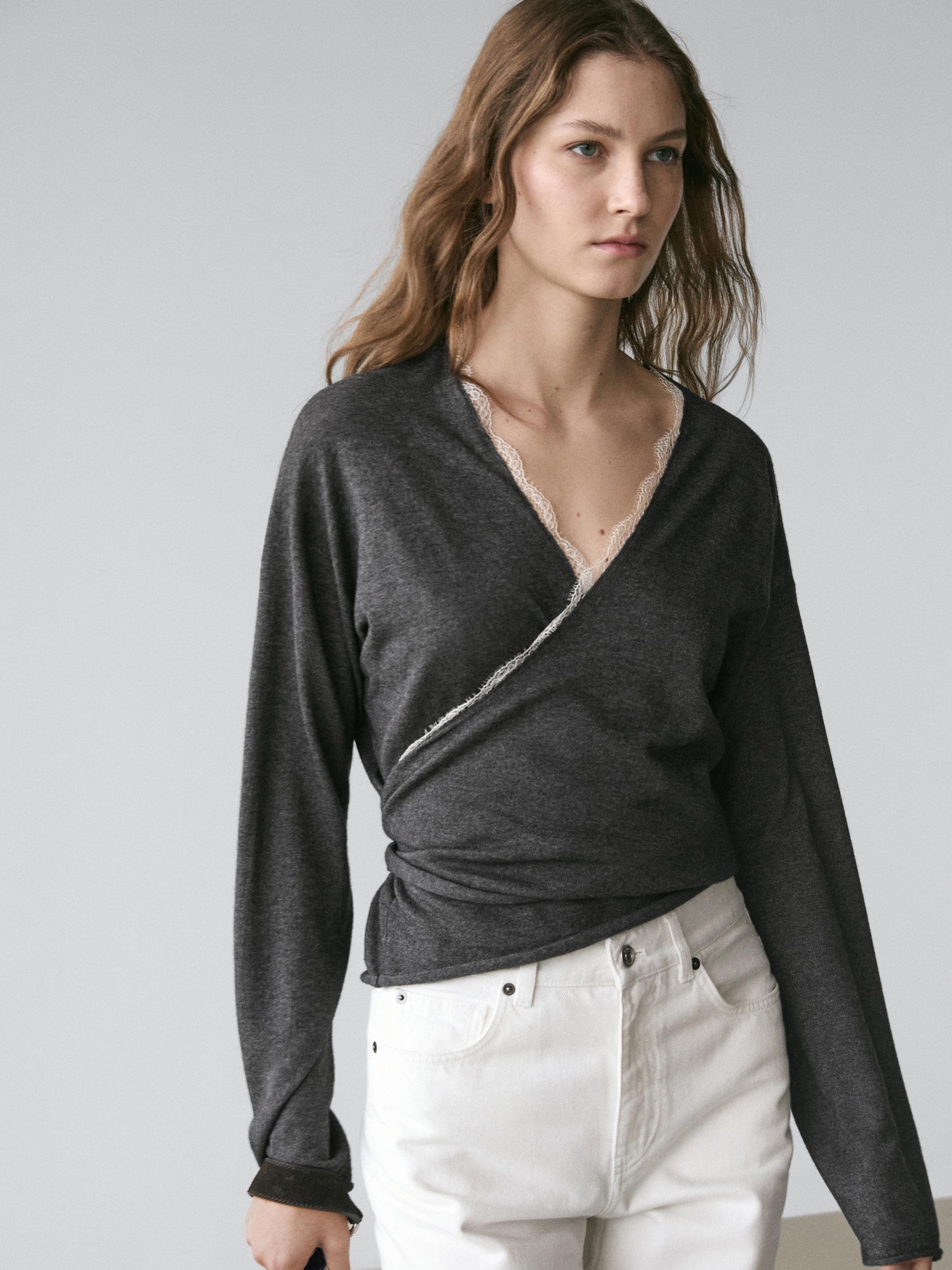 "Medium shot of a charcoal gray wrap cardigan with lace detail on the neckline, paired with white pants."