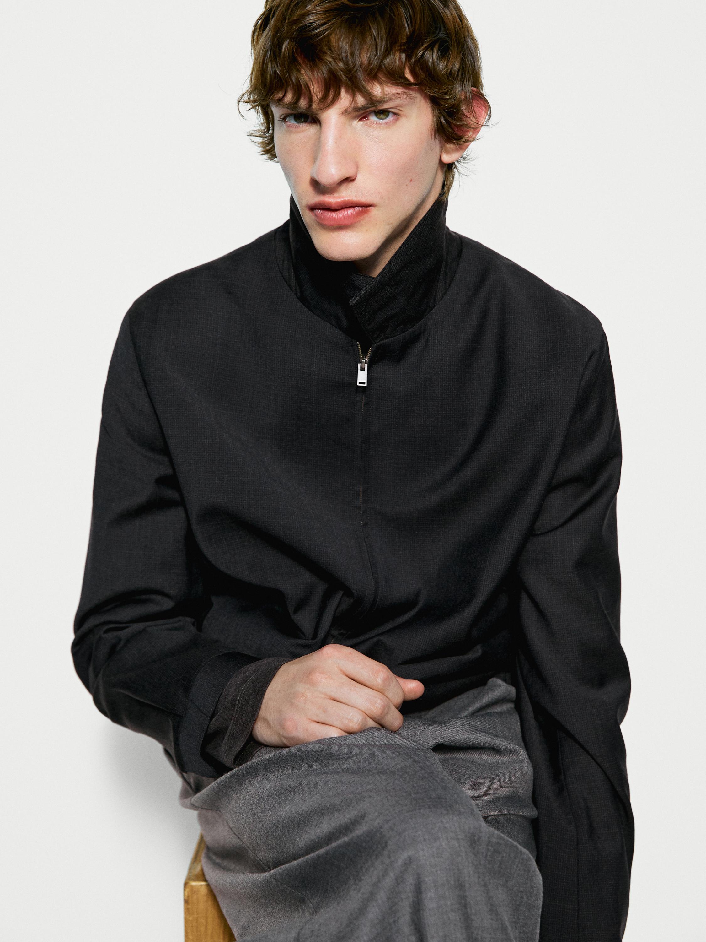 Halflang shot van een zwart jack met rits en hoge kraag, gecombineerd met een grijze broek.