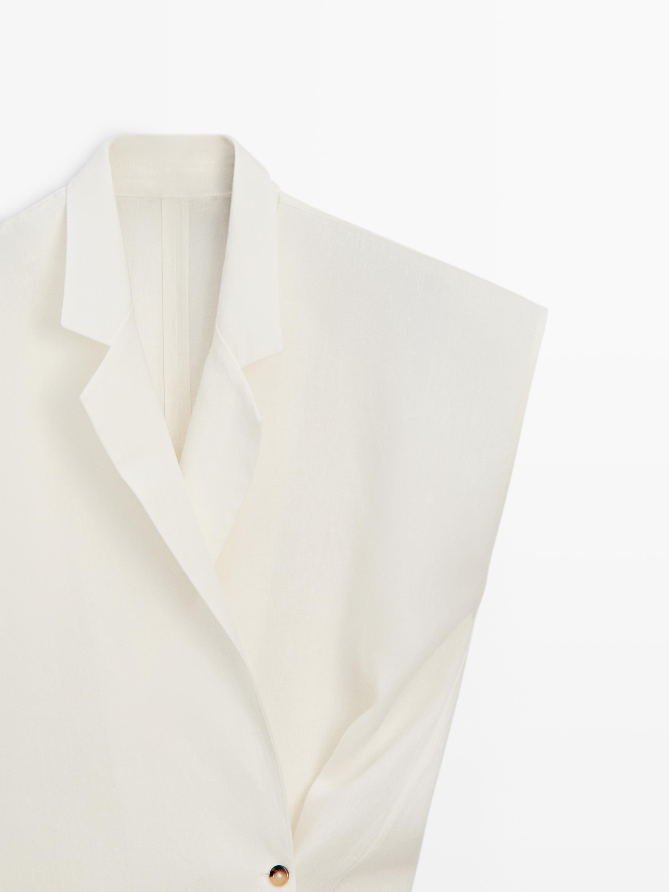 "Detalle de la solapa y botonadura de un blazer blanco roto sin mangas."