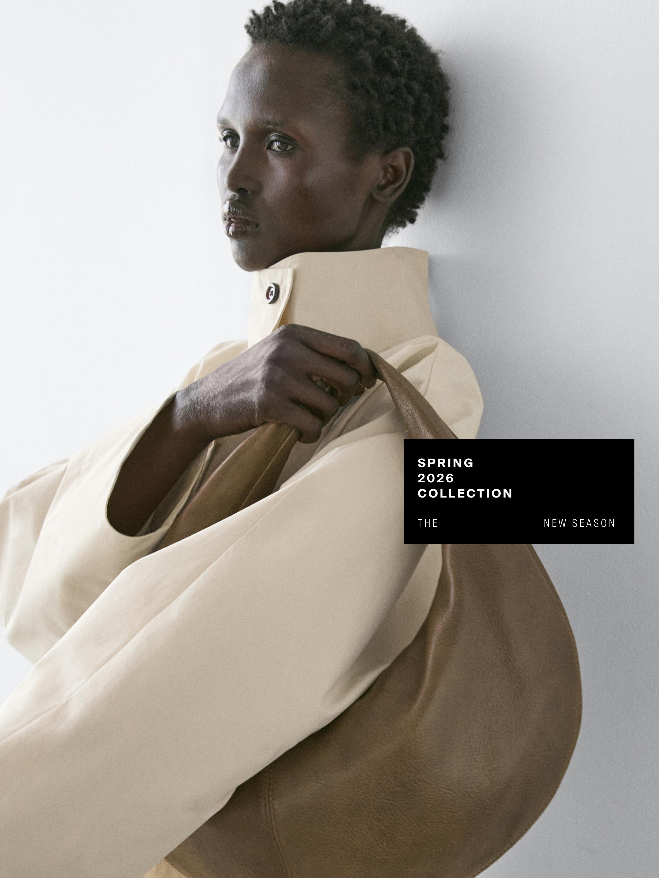 Halbnahe Einstellung einer khakifarbenen Tasche mit dem Text 'SPRING 2026 COLLECTION THE NEW SEASON' und einem beigefarbenen Rollkragenpullover.