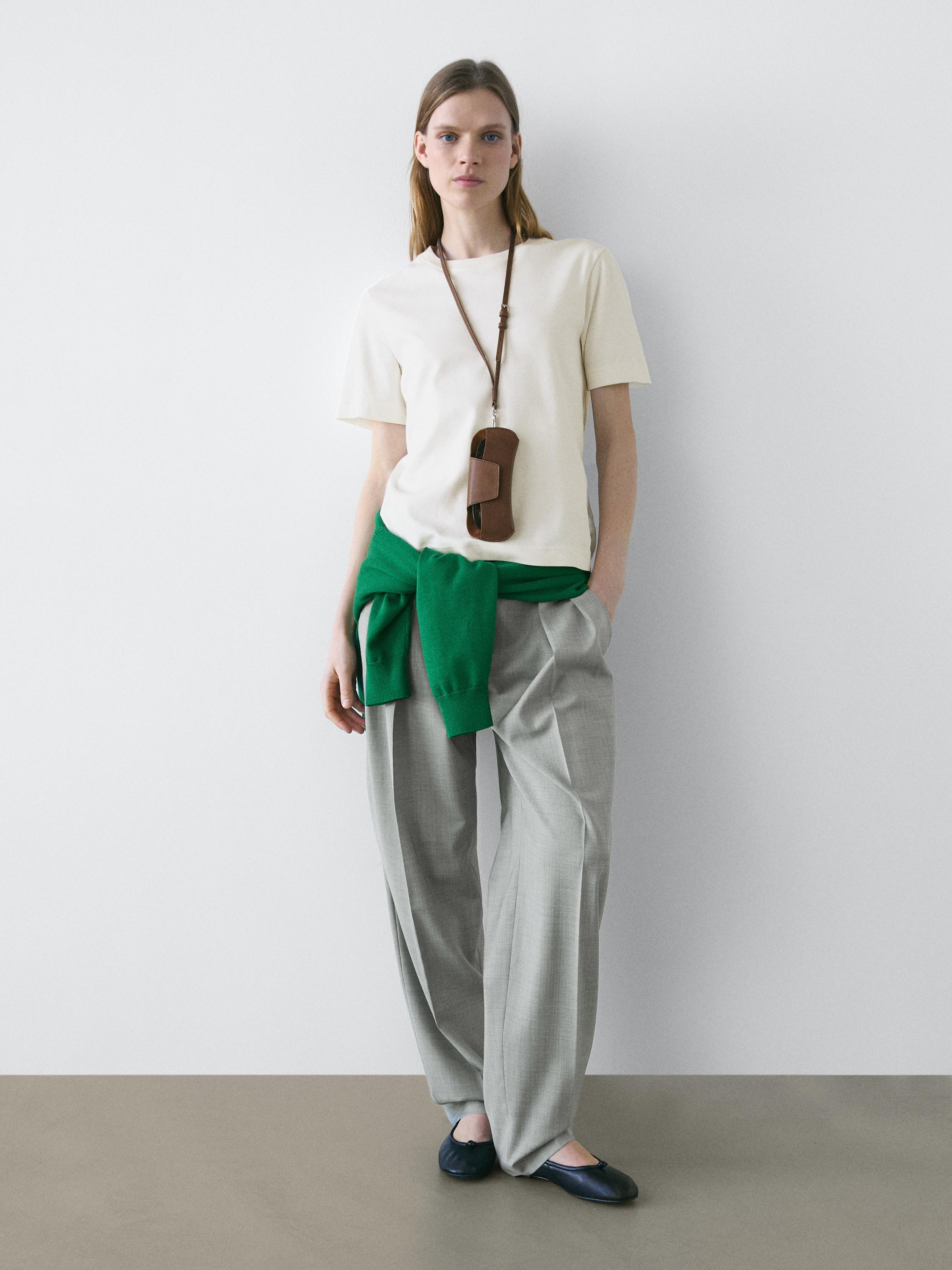 Conjunt de samarreta crua de màniga curta, pantalons grisos amples, jersei verd lligat a la cintura i sabates negres.