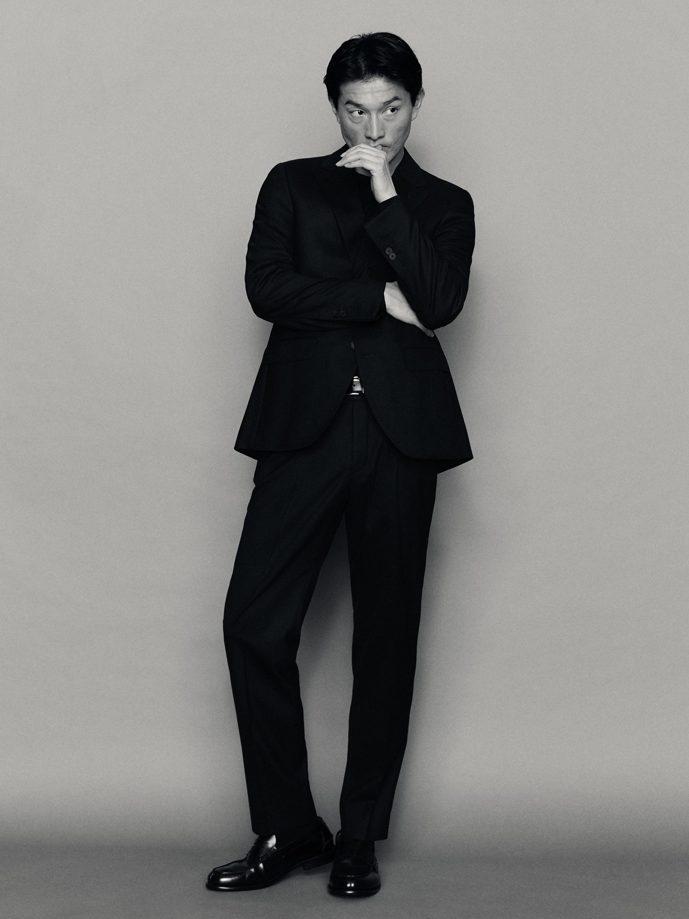 Traje beltz multzoa, bi botoiko jakarekin eta praka zuzenekin. Zapata beltzak ikusgai.