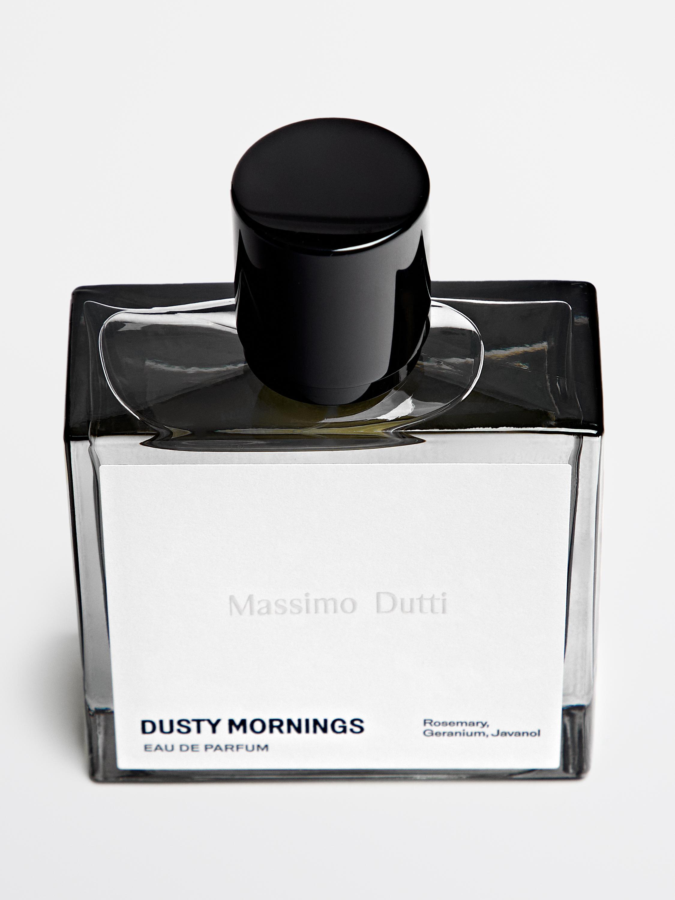 Botella de perfume con texto "DUSTY MORNINGS EAU DE PARFUM" y "Romero, Geranio, Javanol" en etiqueta blanca. Tapa negra.