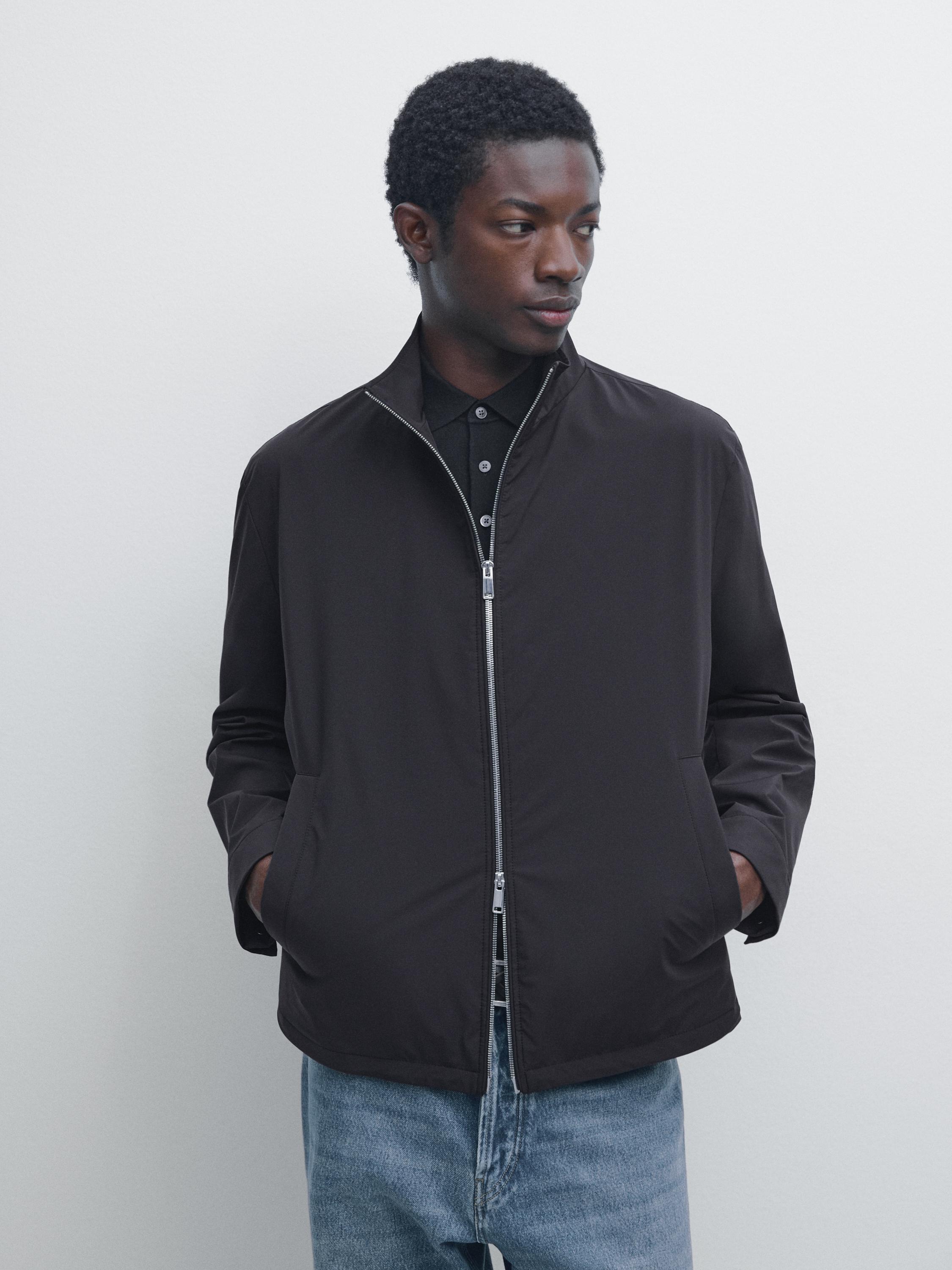 Súprava tmavomodrej bundy s predným zipsom a bočnými vreckami, skombinovaná s modrými džínsovými nohavicami.