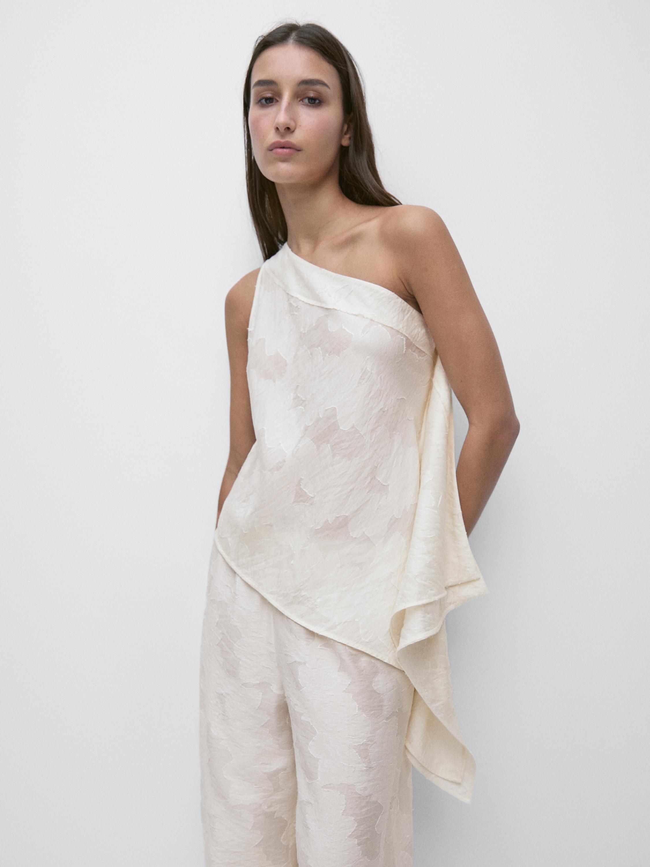 Conjunto de top blanco de escote asimétrico y pantalón a juego con estampado sutil.