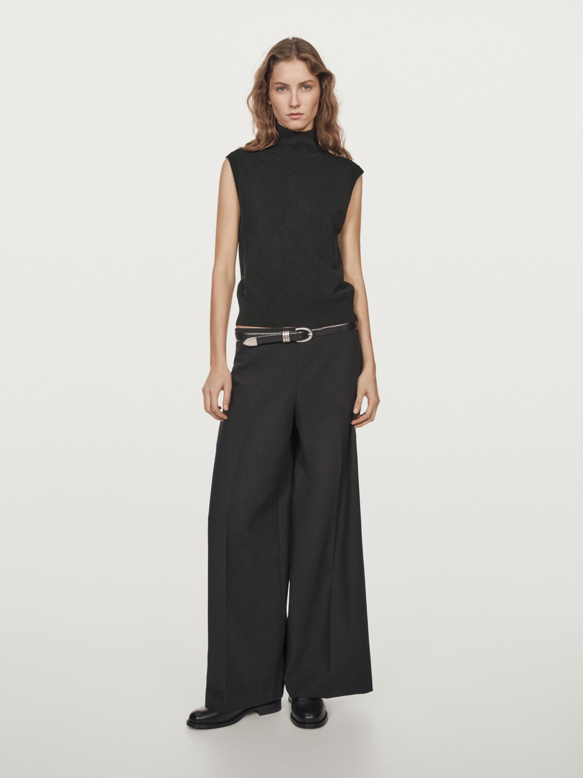 Ensemble de gilet noir sans manches et pantalon large gris avec ceinture métallique.