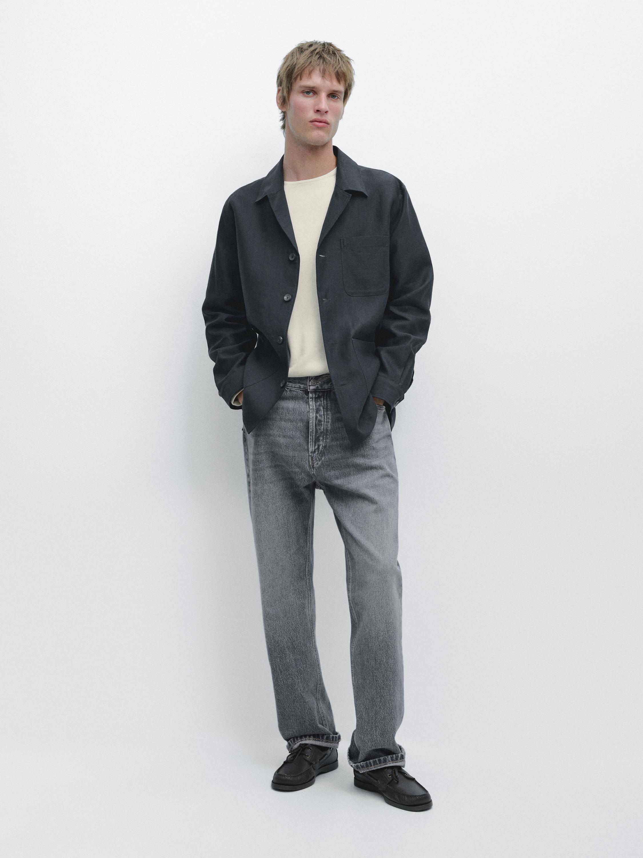 Conjunto de chaqueta negra con bolsillos, camiseta beige y jeans grises rectos.