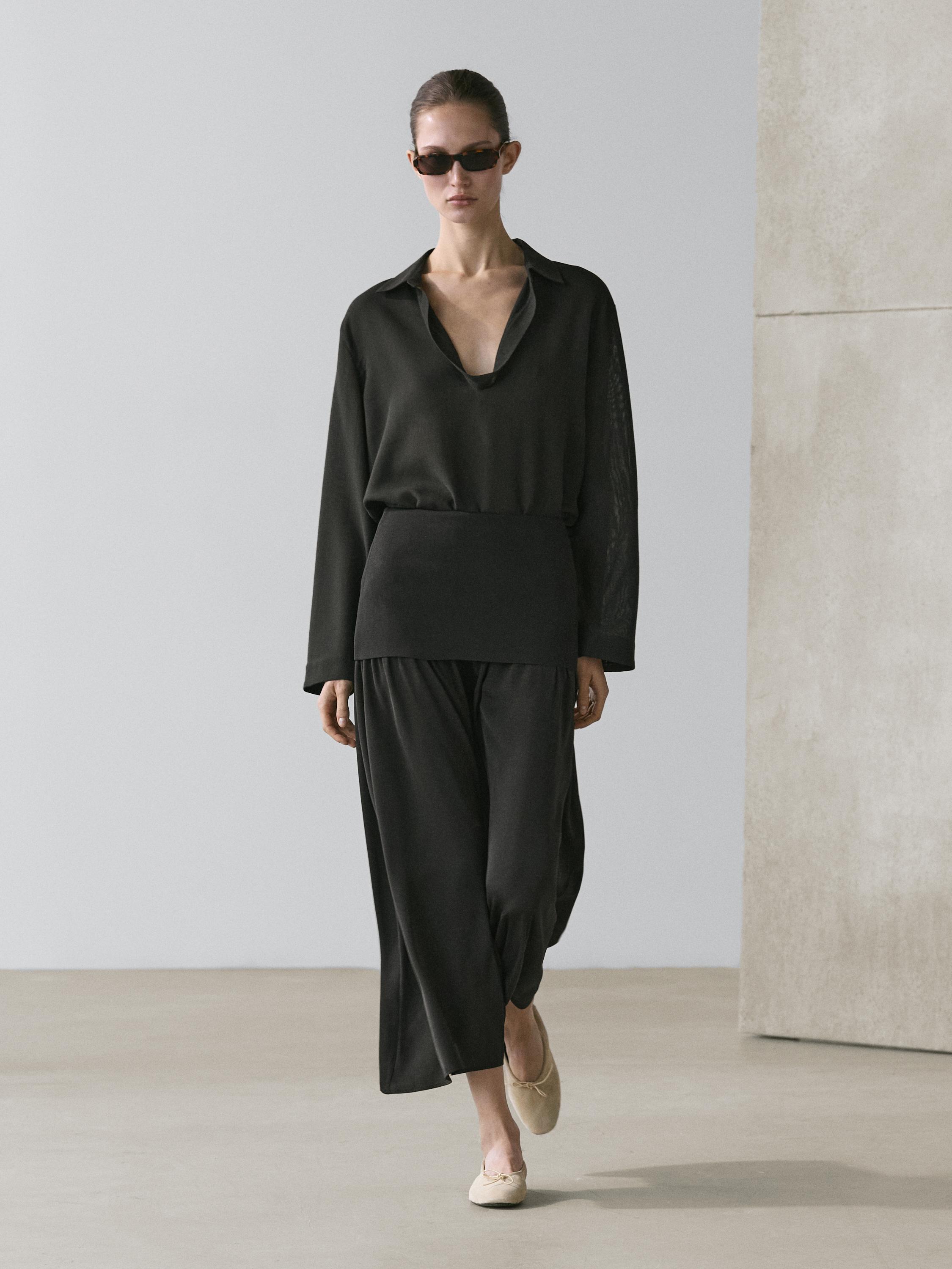 Zwarte blouse met lange mouwen en open kraag en lange zwarte tricot rok.