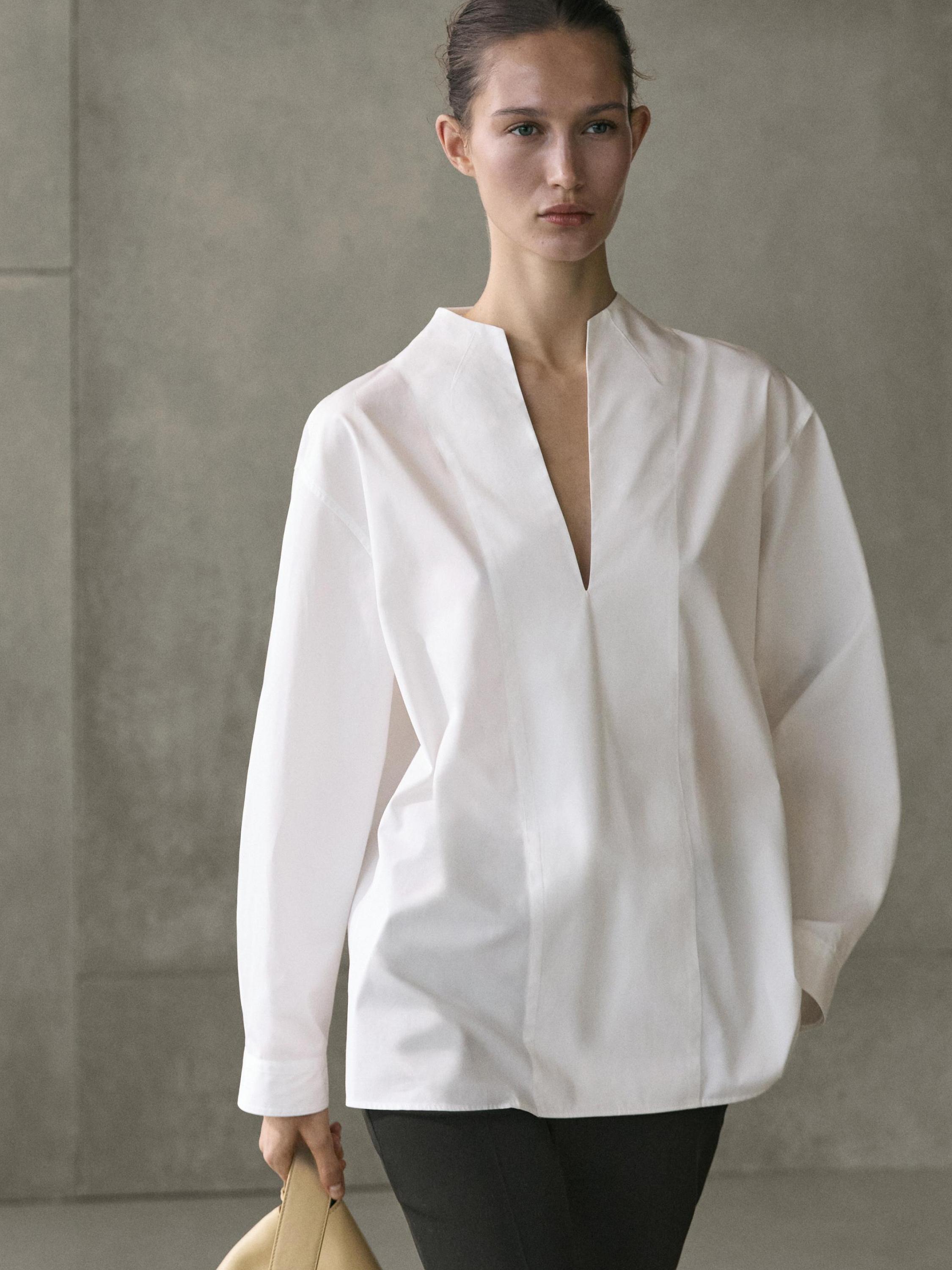 طقم قميص أبيض بأكمام طويلة وياقة مفتوحة، مع بنطلون غامق.