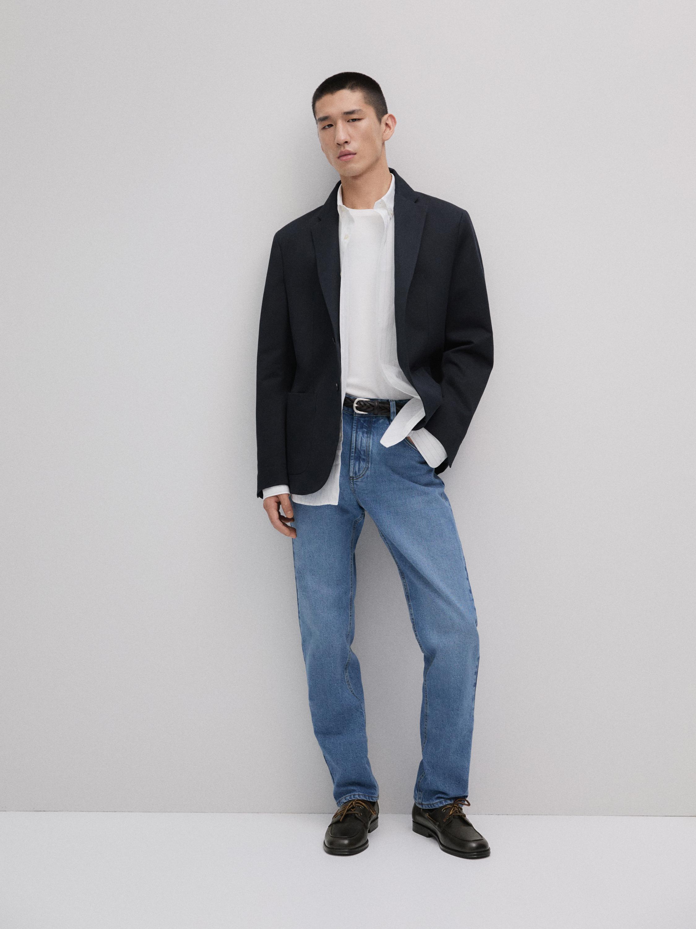 Ensemble composé d'une veste noire, d'une chemise blanche, d'un jean bleu et de chaussures noires.