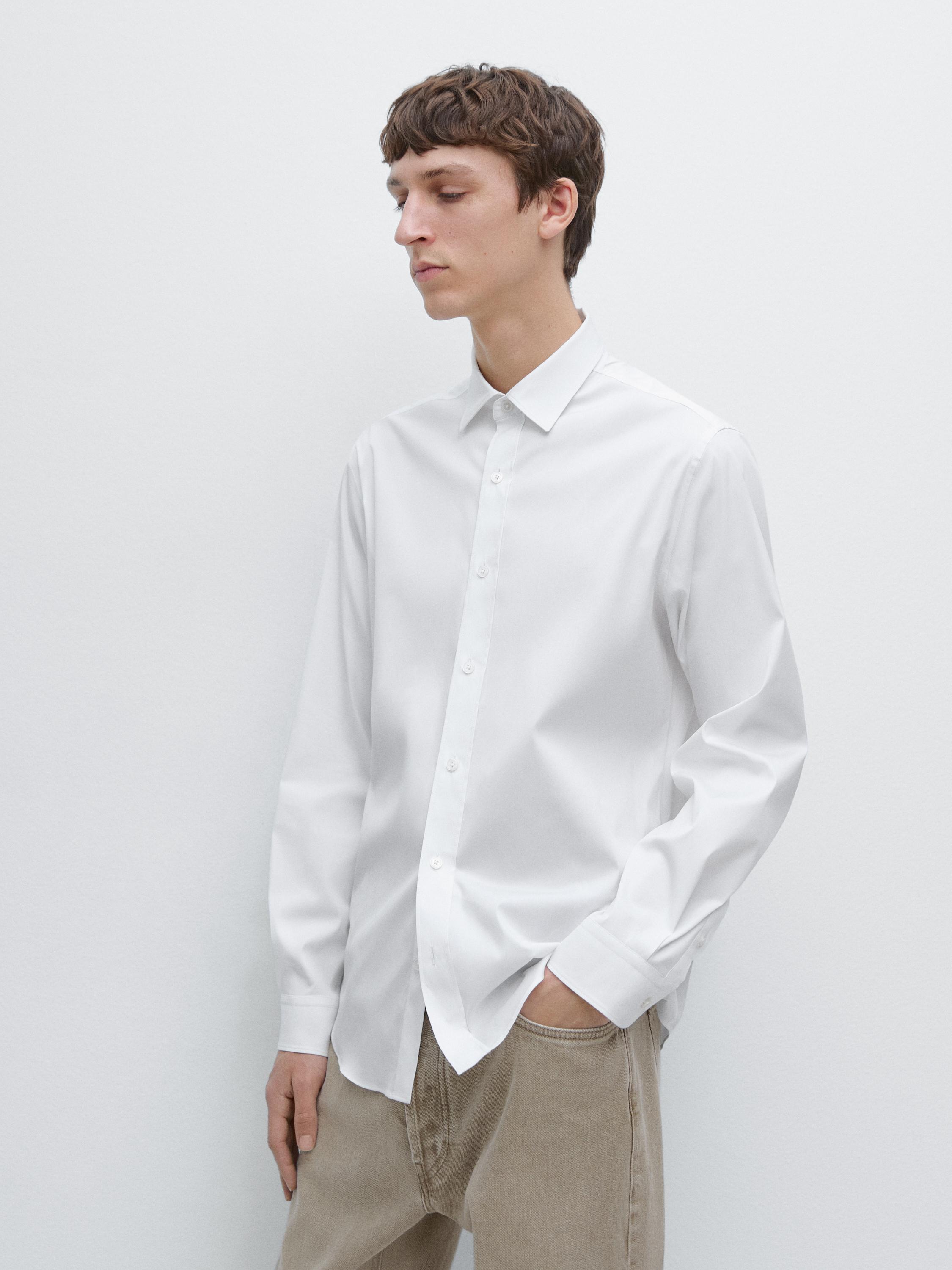 Completo composto da camicia bianca a maniche lunghe con bottoni e colletto classico, abbinata a pantaloni beige.