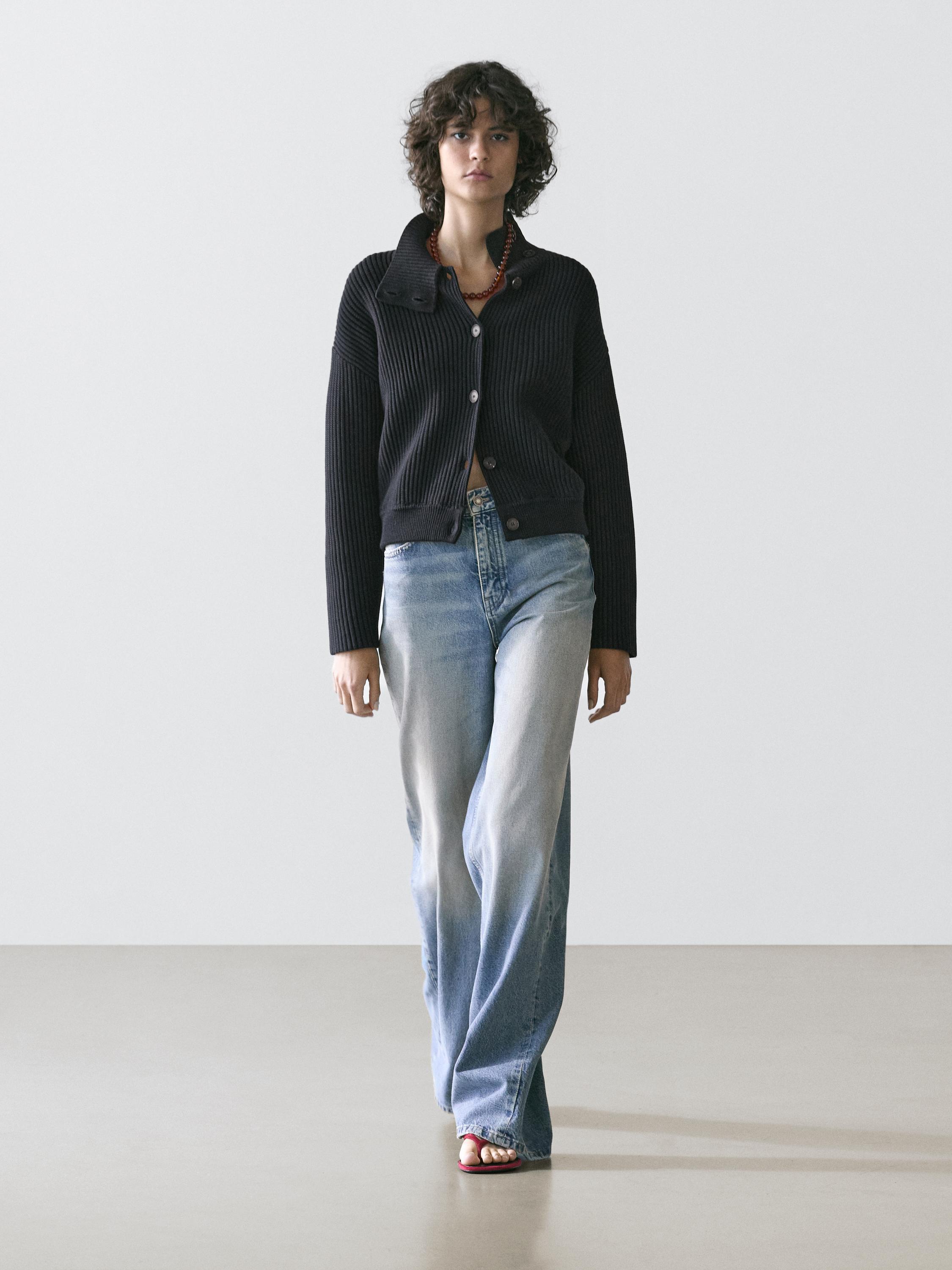 Conjunto de cárdigan azul-marinho de malha com gola alta e botões, e jeans azul-claro de corte reto.