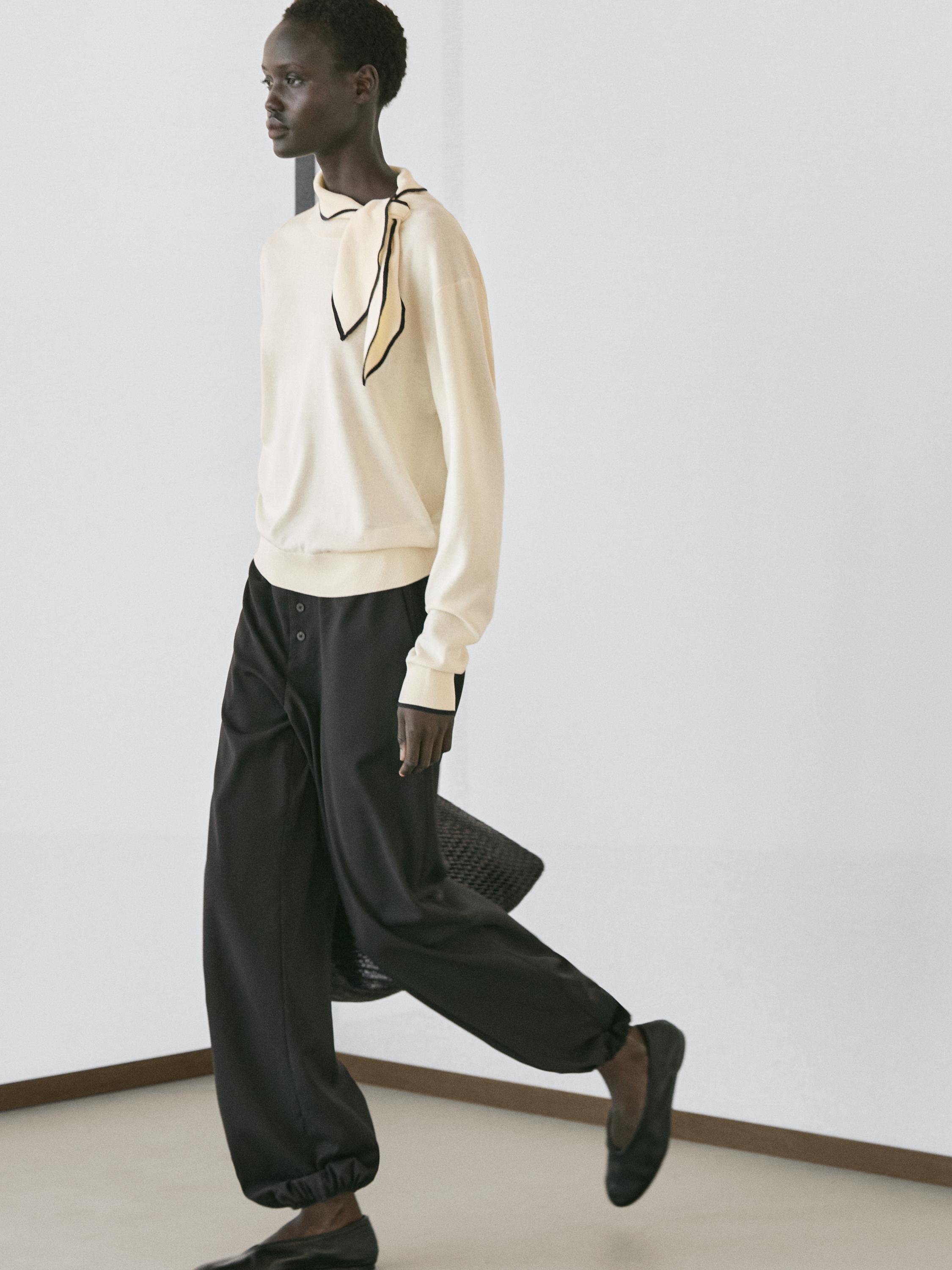 Ensemble pull écru avec détail foulard et pantalon ample noir avec poignets élastiques.