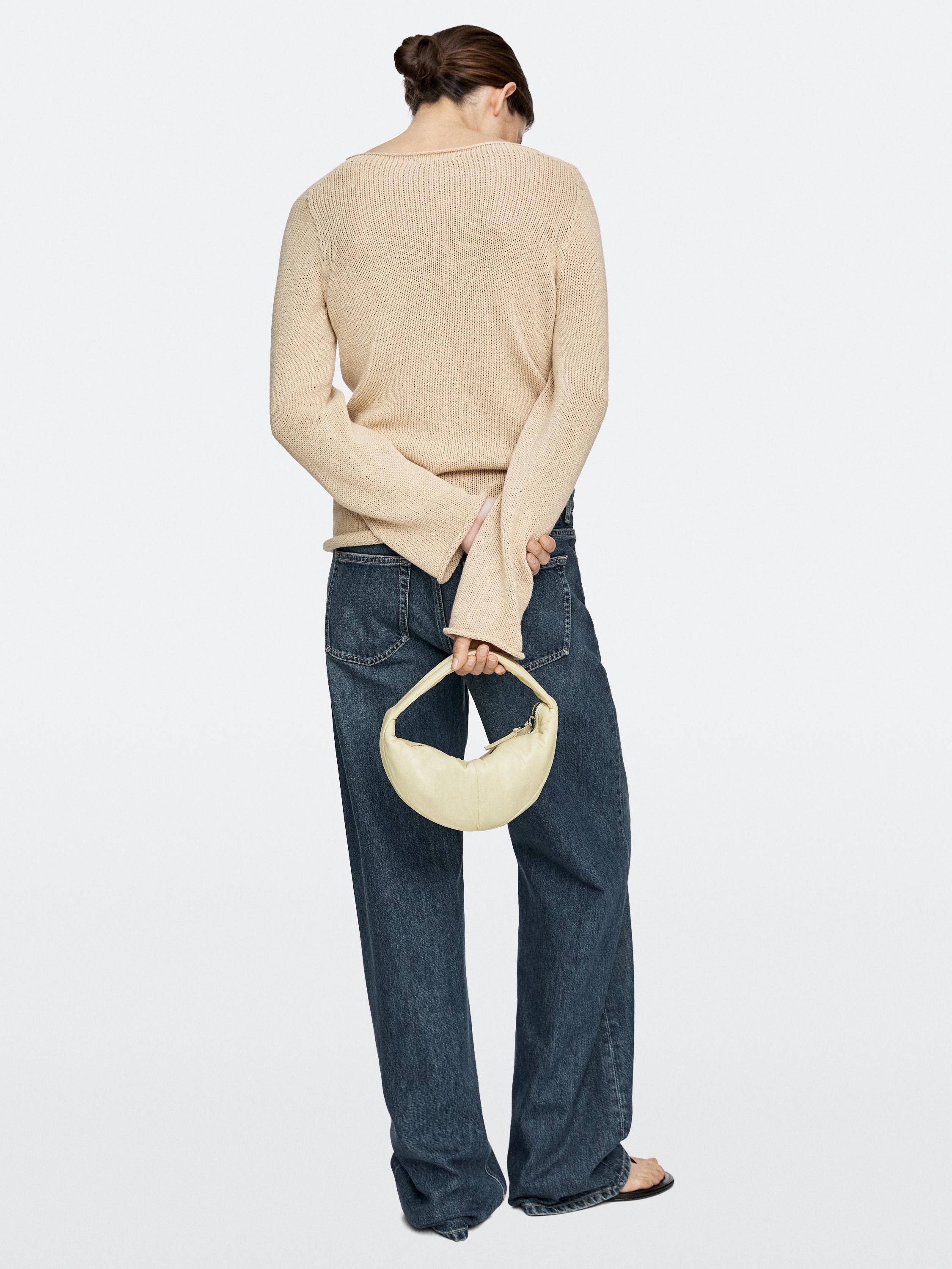 Set van beige trui, donkerblauwe jeans en kleine witte tas.