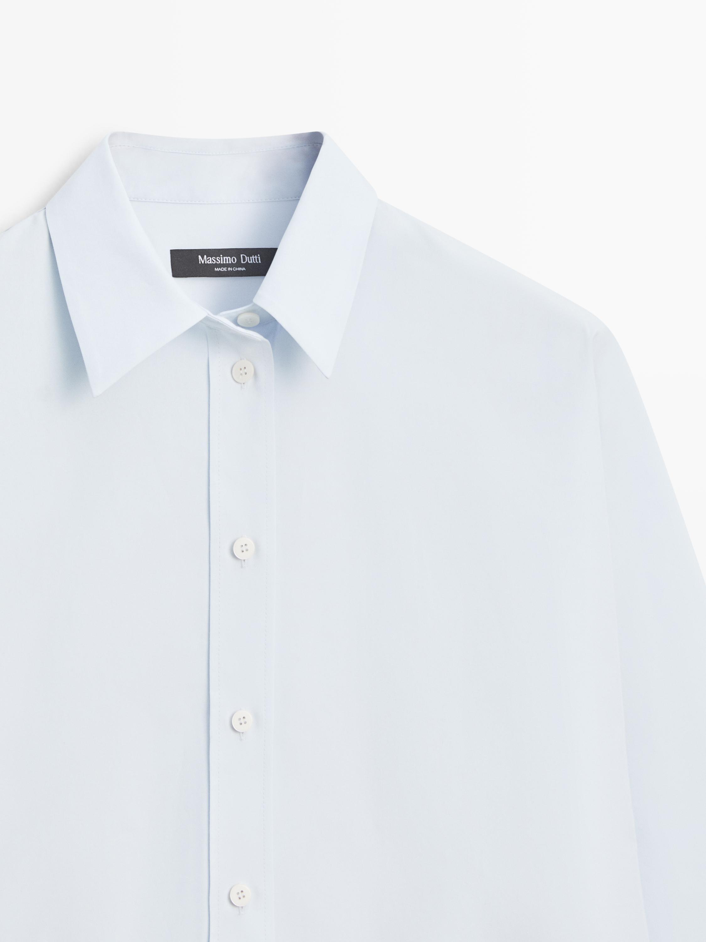 Klasik yakalı ve önü düğmeli açık mavi gömleğin orta çekimi. Üzerinde 'Massimo Dutti' yazan etiket görünür.