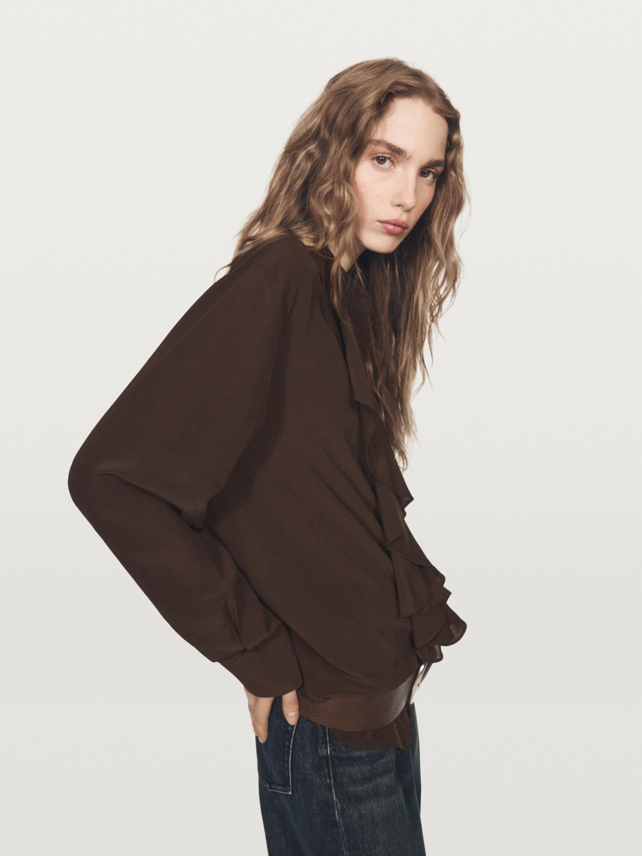 Plano medio de blusa marrón con volantes en el frente y mangas largas.