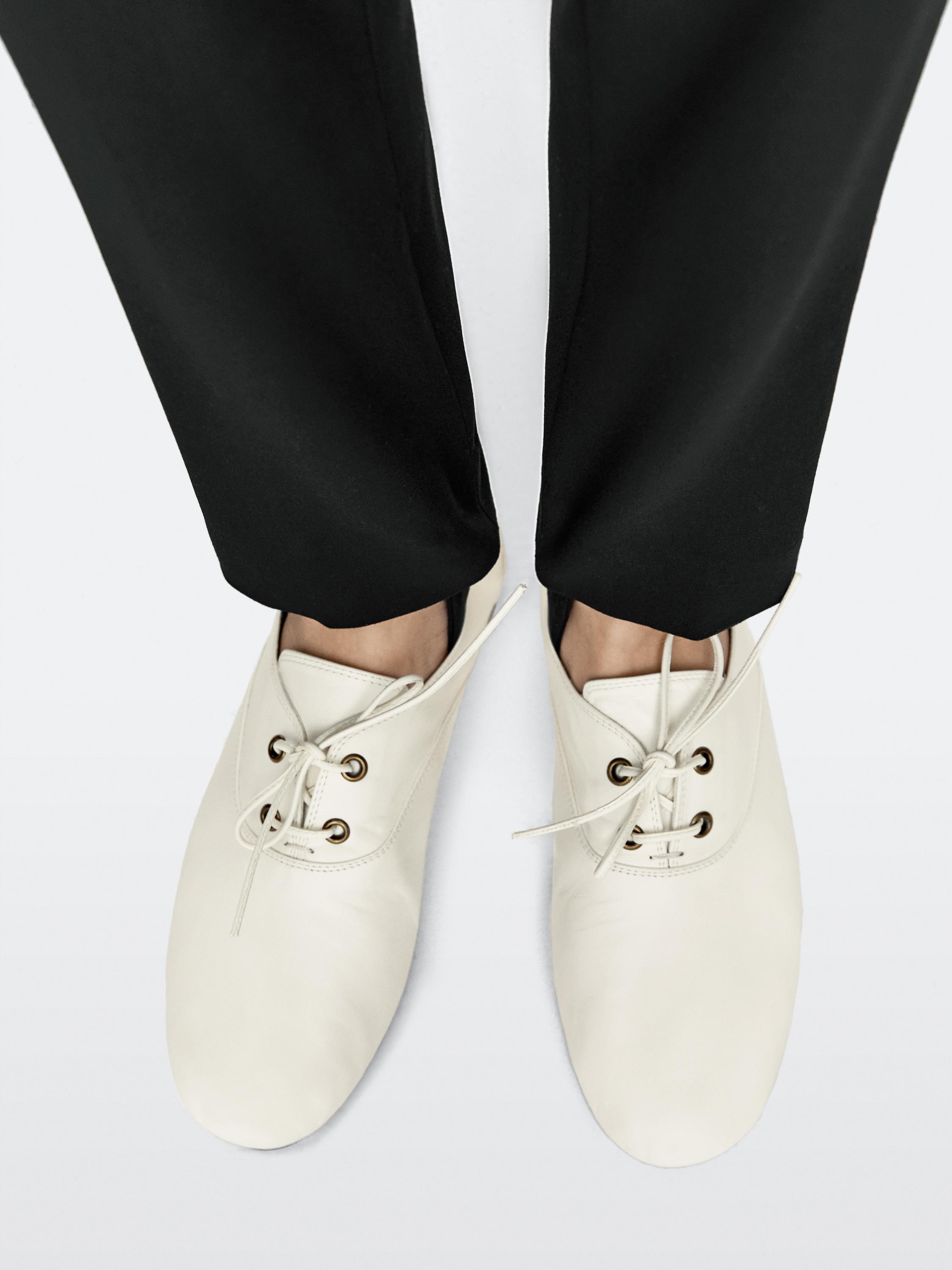 Σετ λευκά flat παπούτσια με κορδόνια και μεταλλικές οπές, ιδωμένα από πάνω.