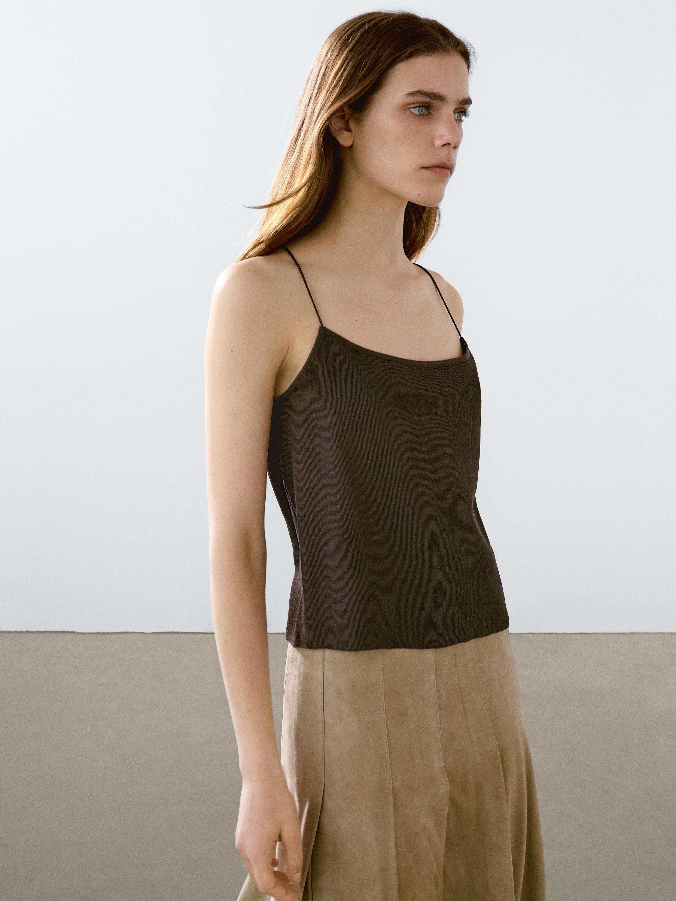 لقطة متوسطة لتوب بحمالات رفيعة بلون داكن مع تنورة بيج مكشكشة.