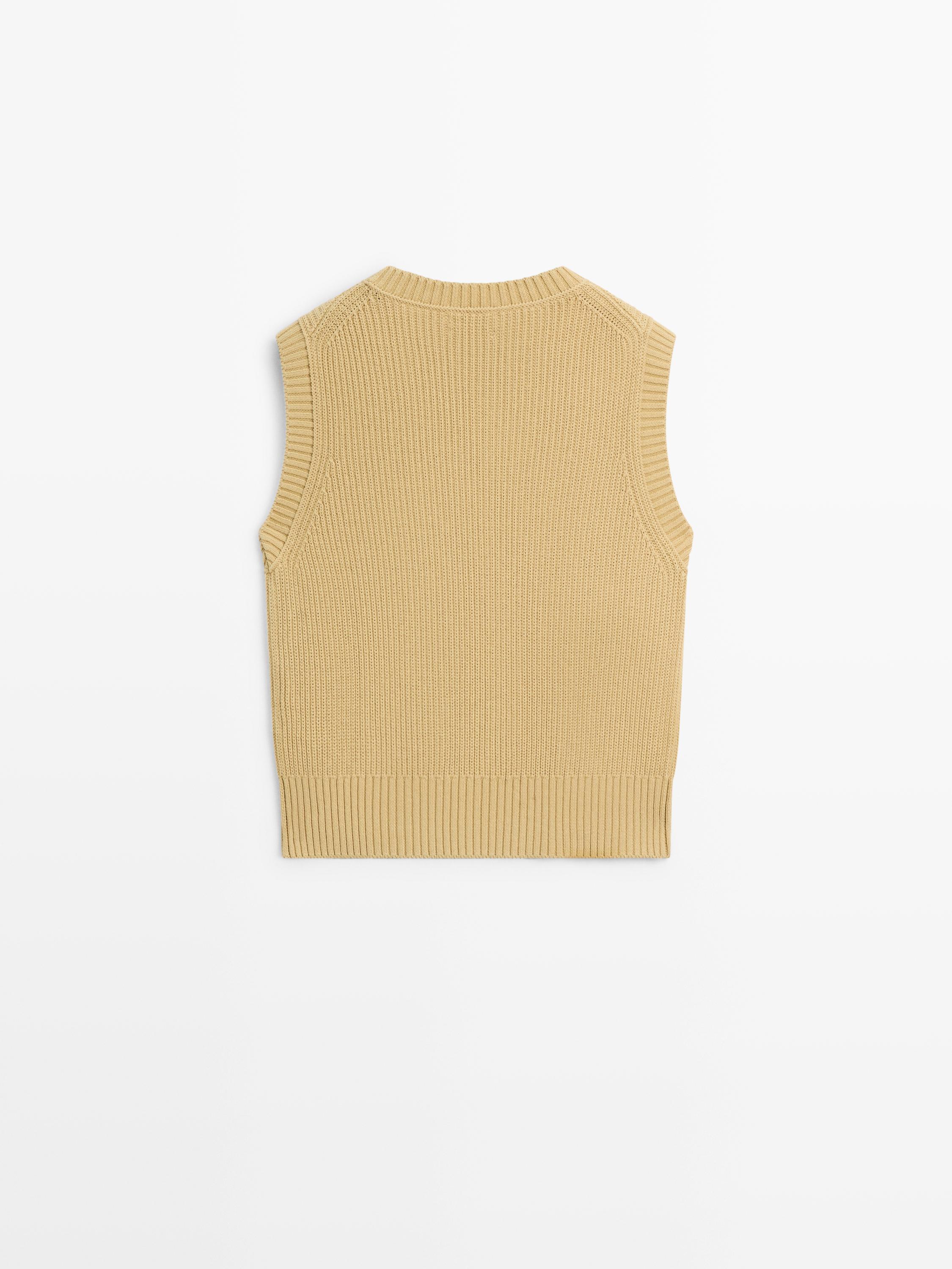 Vista posterior d'armilla de punt en color beix, sense mànigues, amb coll rodó i rivet acanalat a la vora.