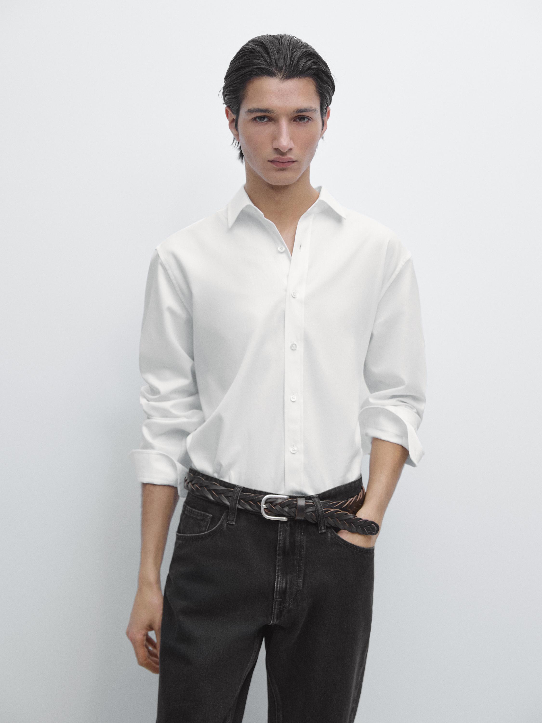 Completo di camicia bianca a maniche lunghe con abbottonatura frontale e pantaloni scuri con cintura intrecciata.