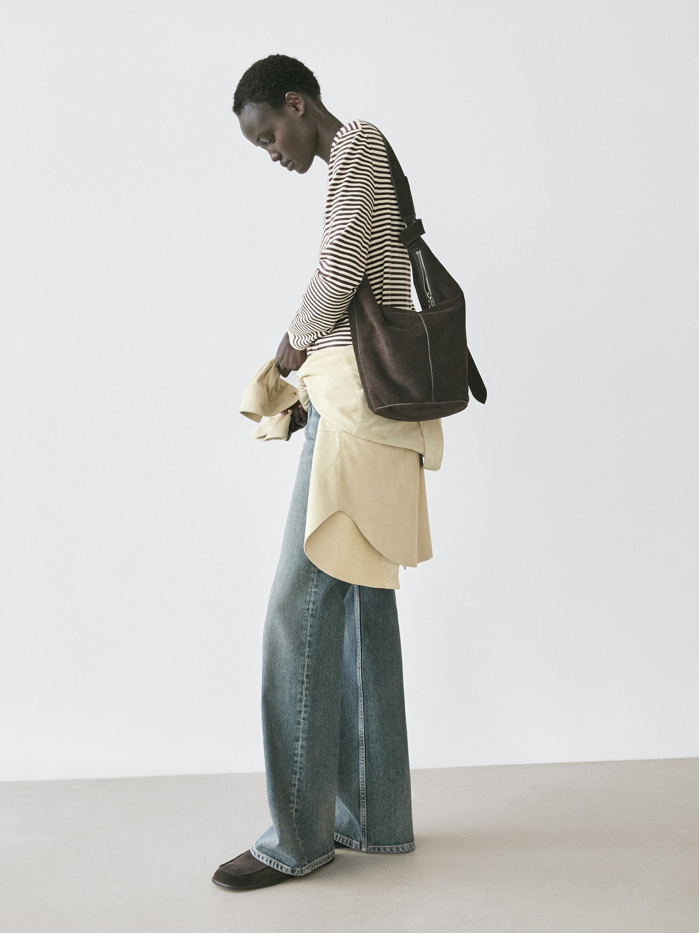 Ensemble composé d'un pull rayé écru et noir, d'un jean large bleu, d'un sac marron et de chaussures foncées.