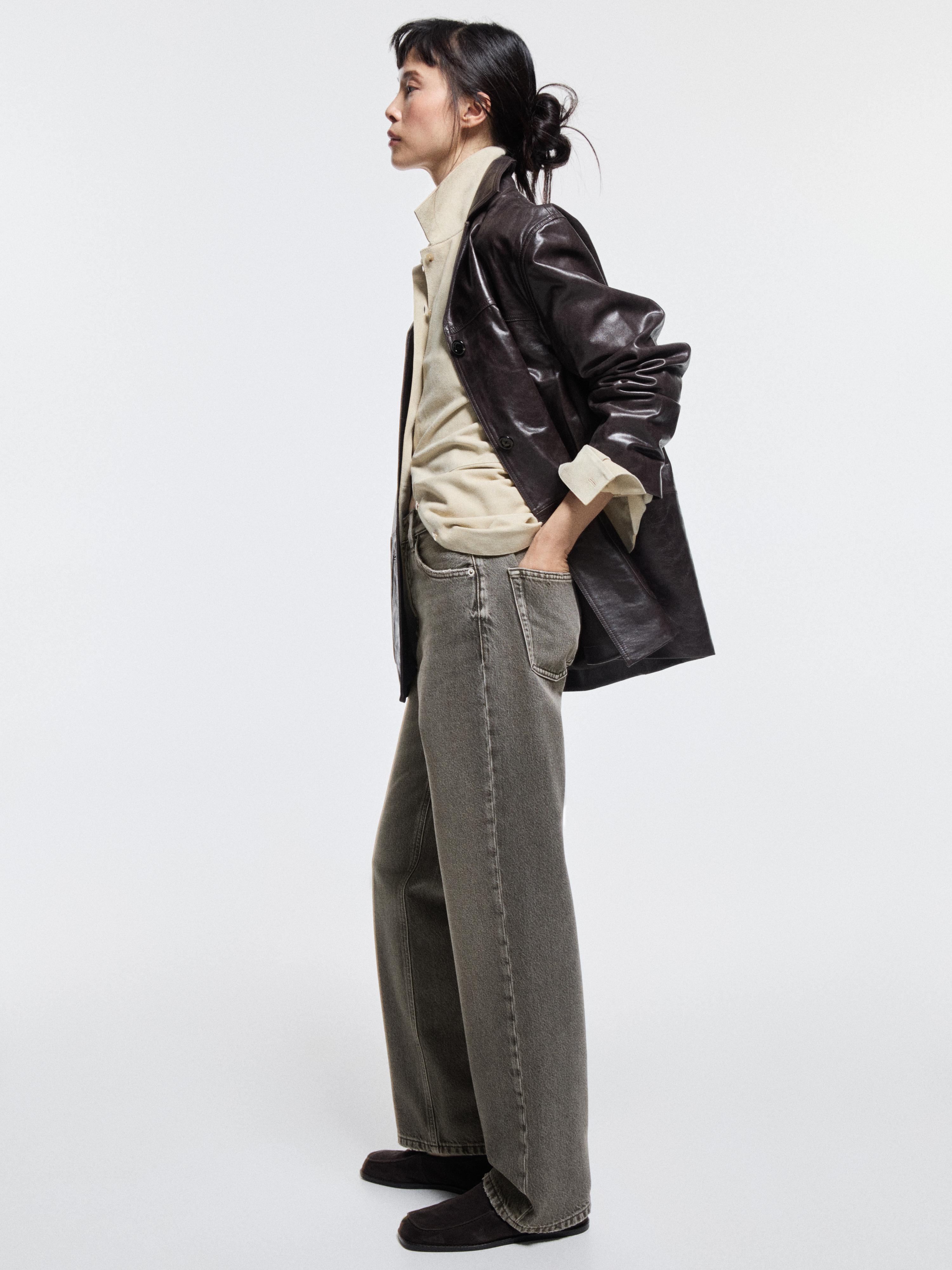 Doğal gri kot takımı, balon fit kesimli ve orta bel, bej gömlek ve koyu renk kaban. Yan cepleri görünür.